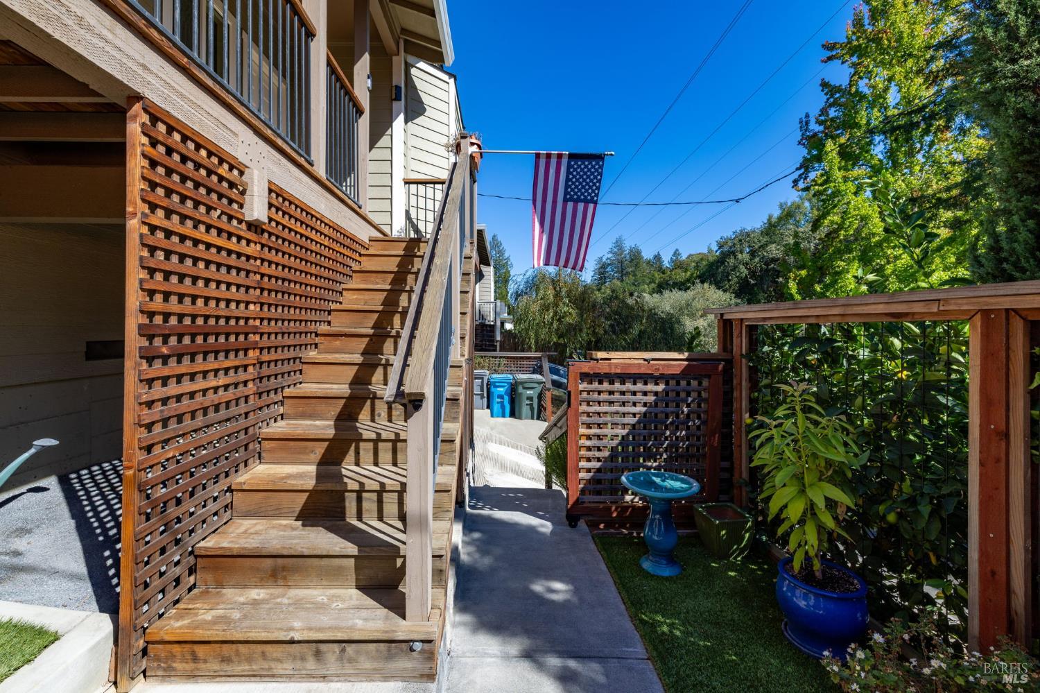 Home exterior with wooden stairs, lattice railings, potted plants, and an American flag.