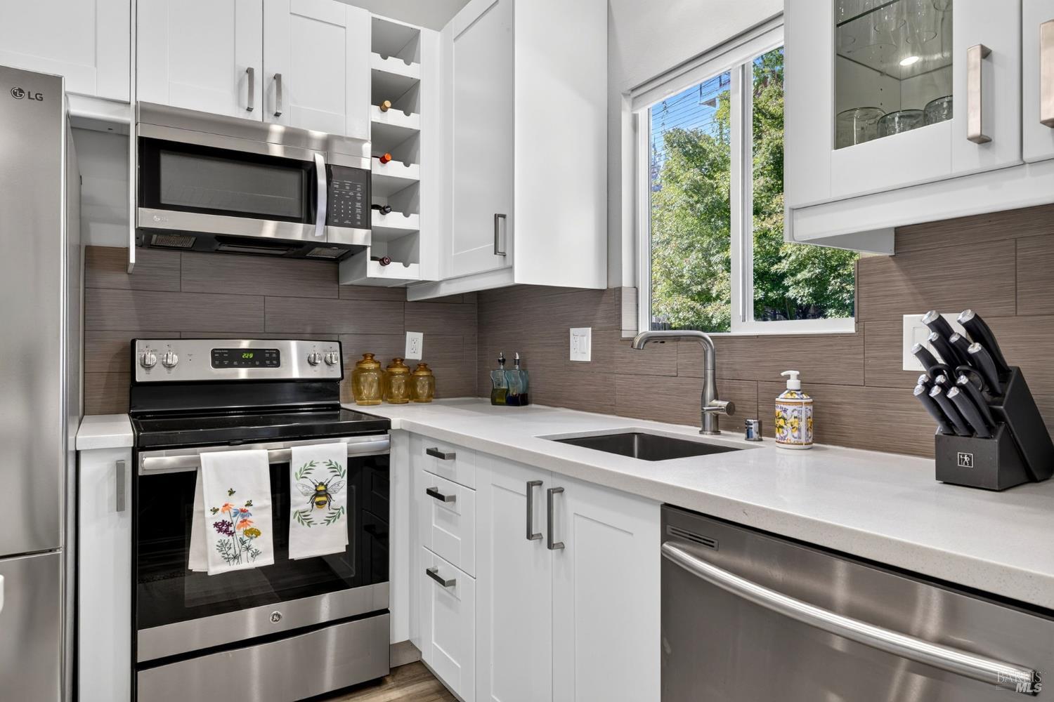 Modern kitchen with white cabinets, stainless steel appliances, and a window above the sink.