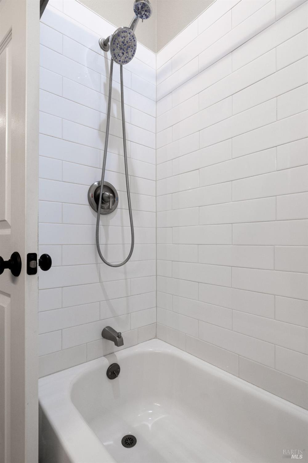 White subway-tile bathtub and shower with a handheld showerhead and brushed-metal fixtures.