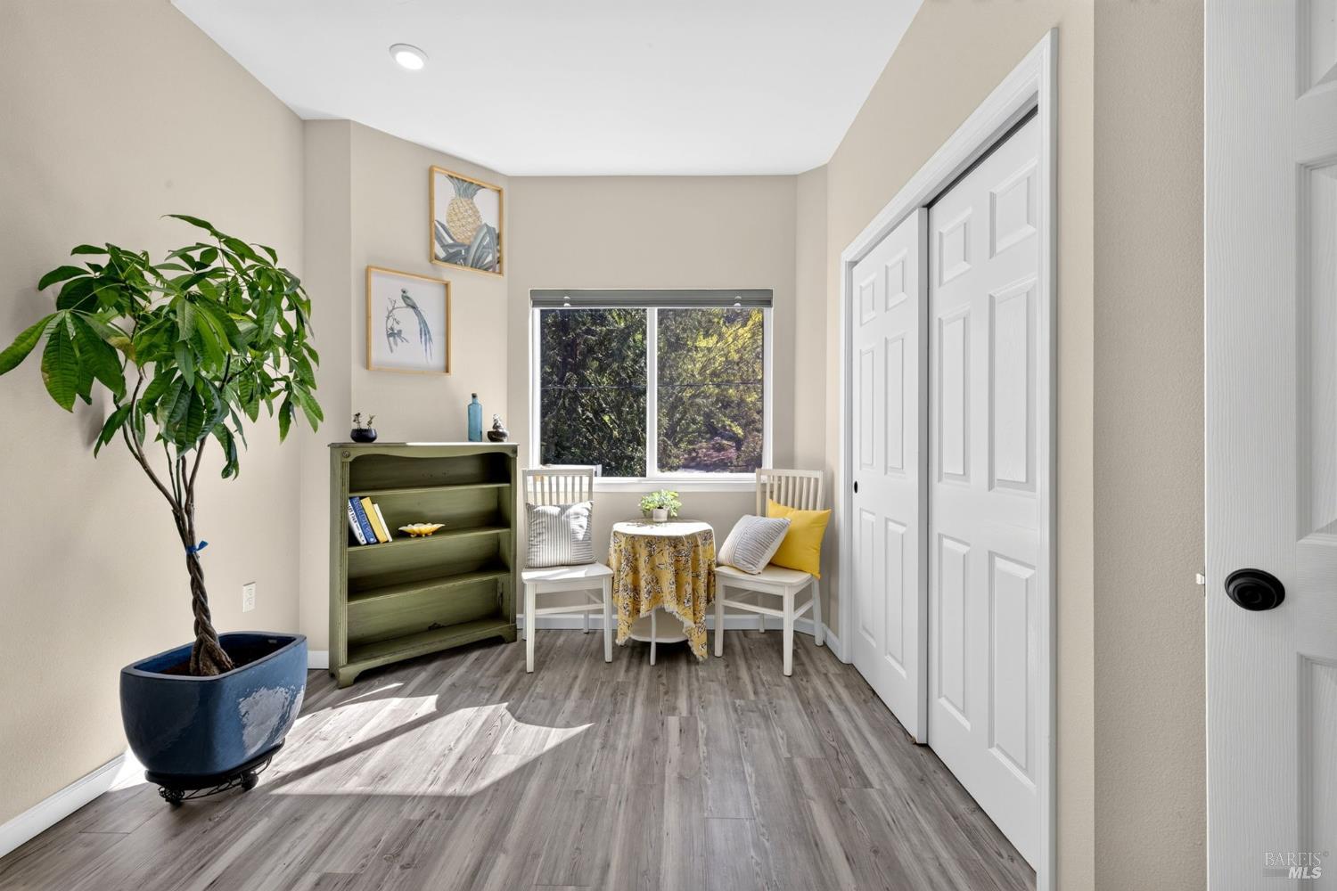 Seating nook with white chairs and a small table beside a window and green bookcase.