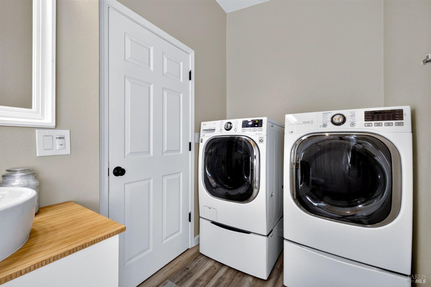 Laundry room with front-loading washer and dryer beside a wood countertop.