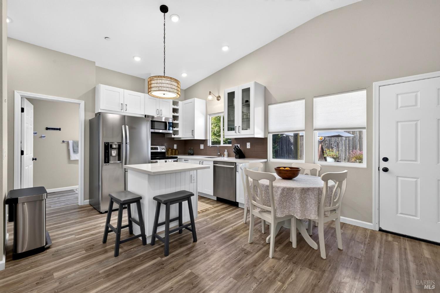 Kitchen and dining area with a white island, stainless steel appliances, and a round table by the windows.