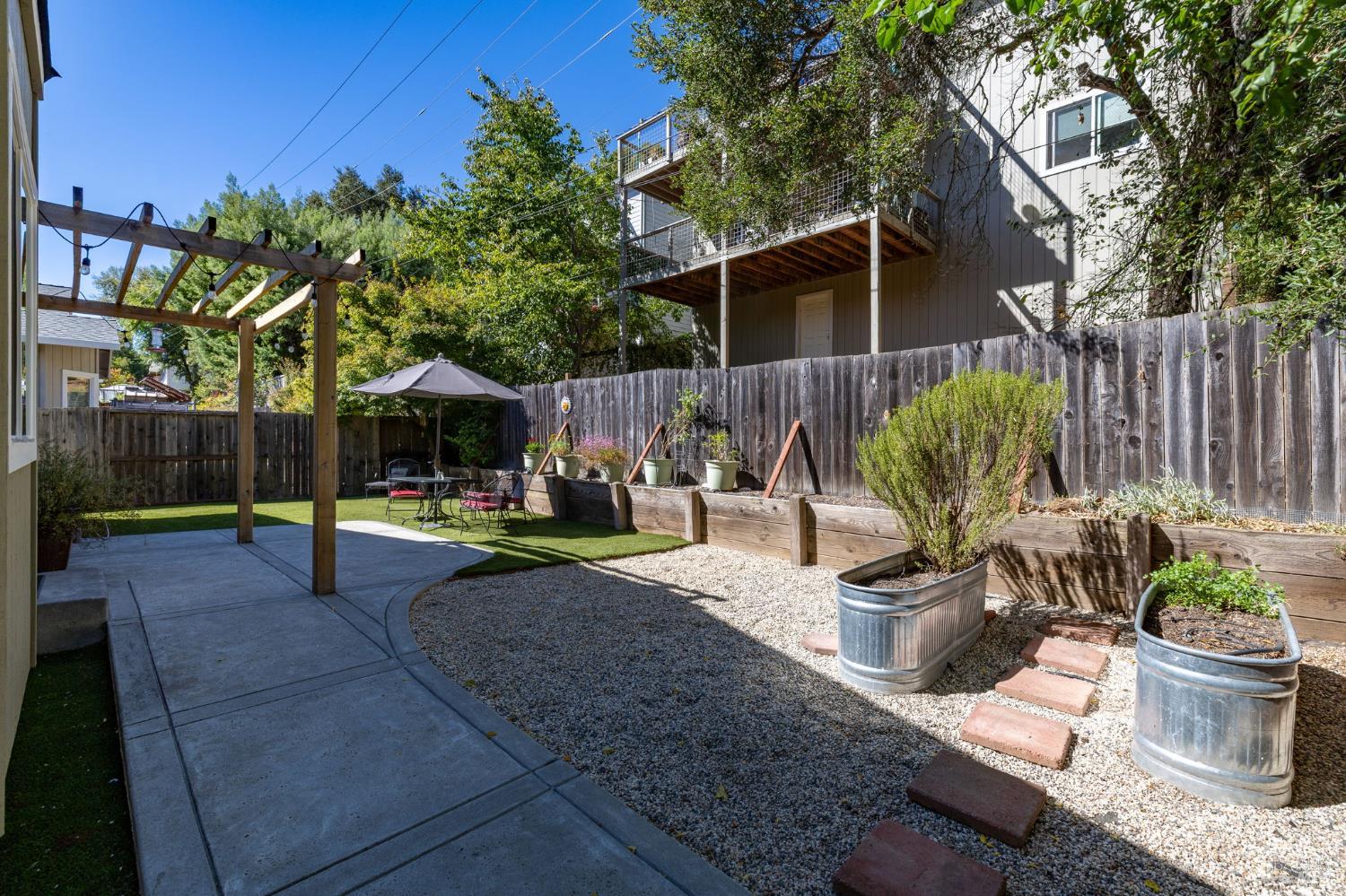 Backyard patio with a pergola, gravel path, raised garden beds, and an elevated deck.