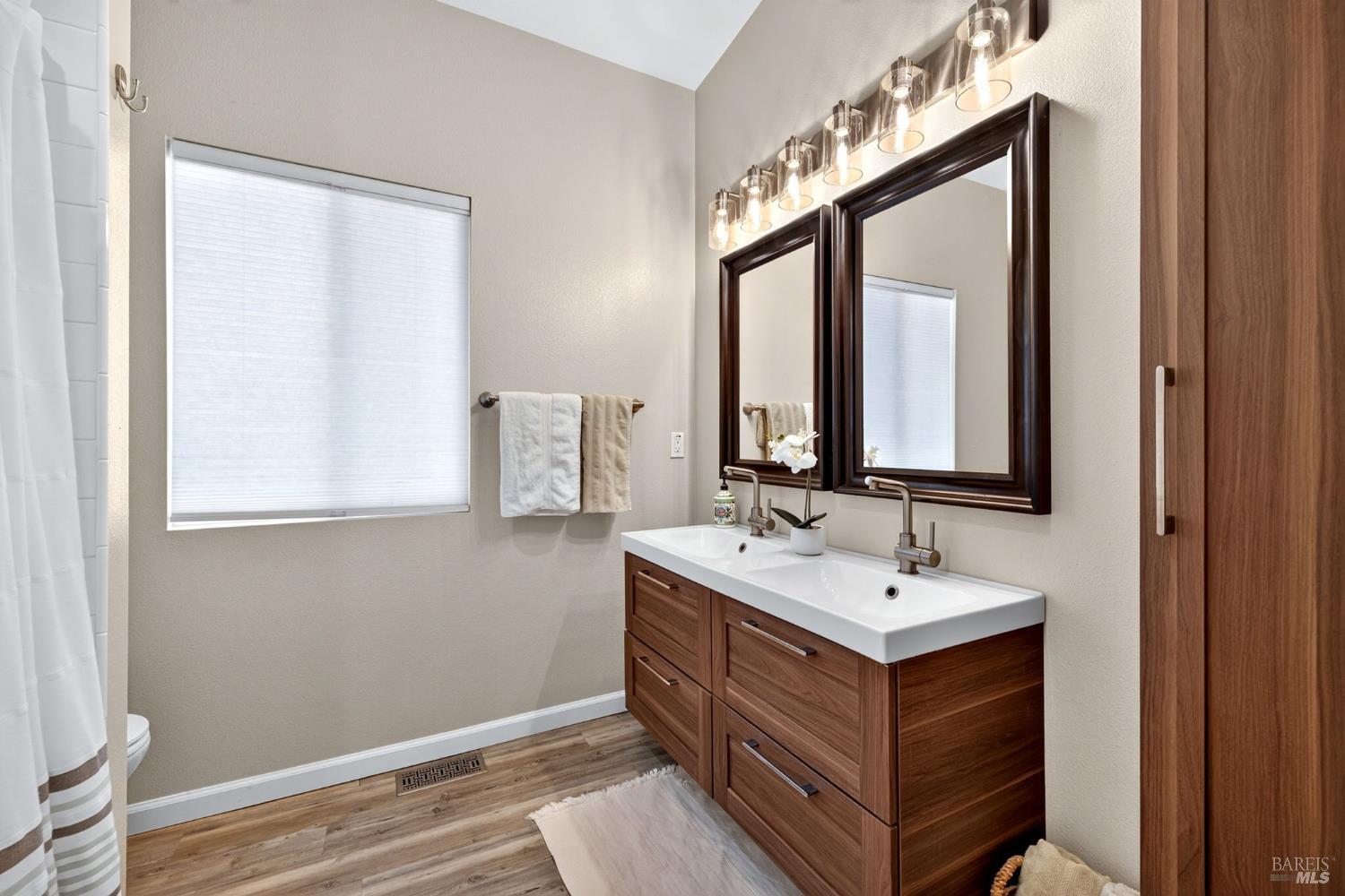 Bathroom with a double-sink wood vanity, dark-framed mirrors, and a row of glass sconces.