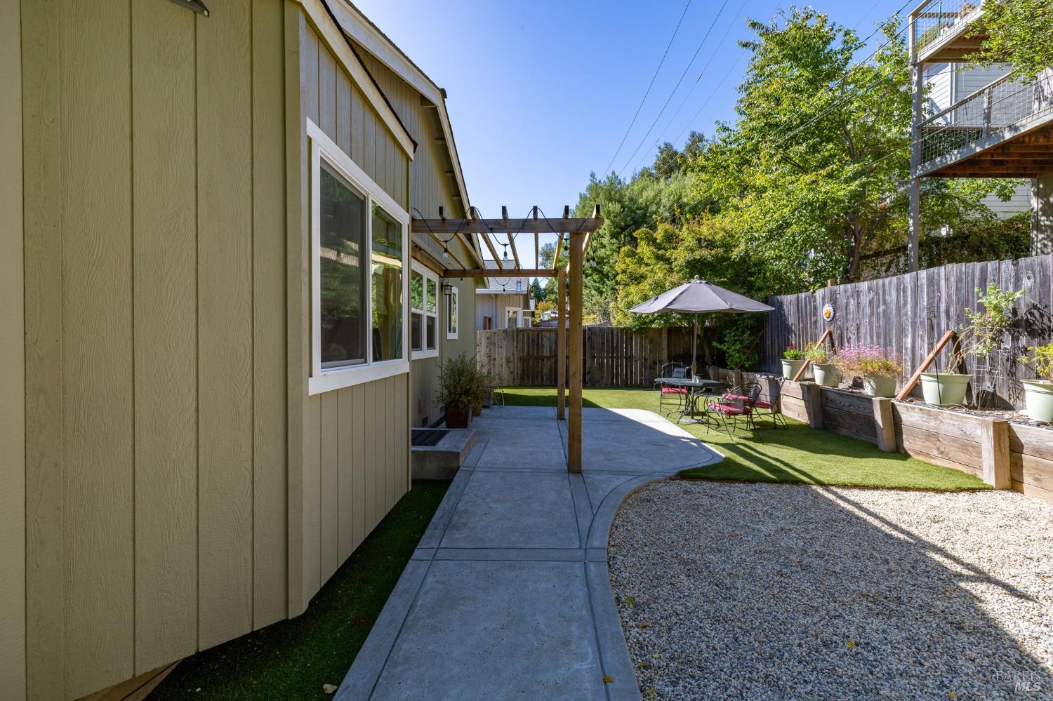 Backyard patio with a pergola, outdoor dining set, raised garden beds, and gravel area.