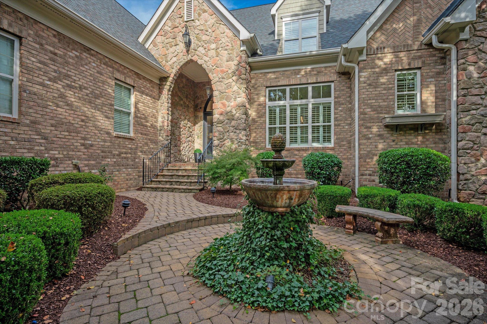 Brick home with a stone-arched entrance, courtyard fountain, and curved paver walkway.