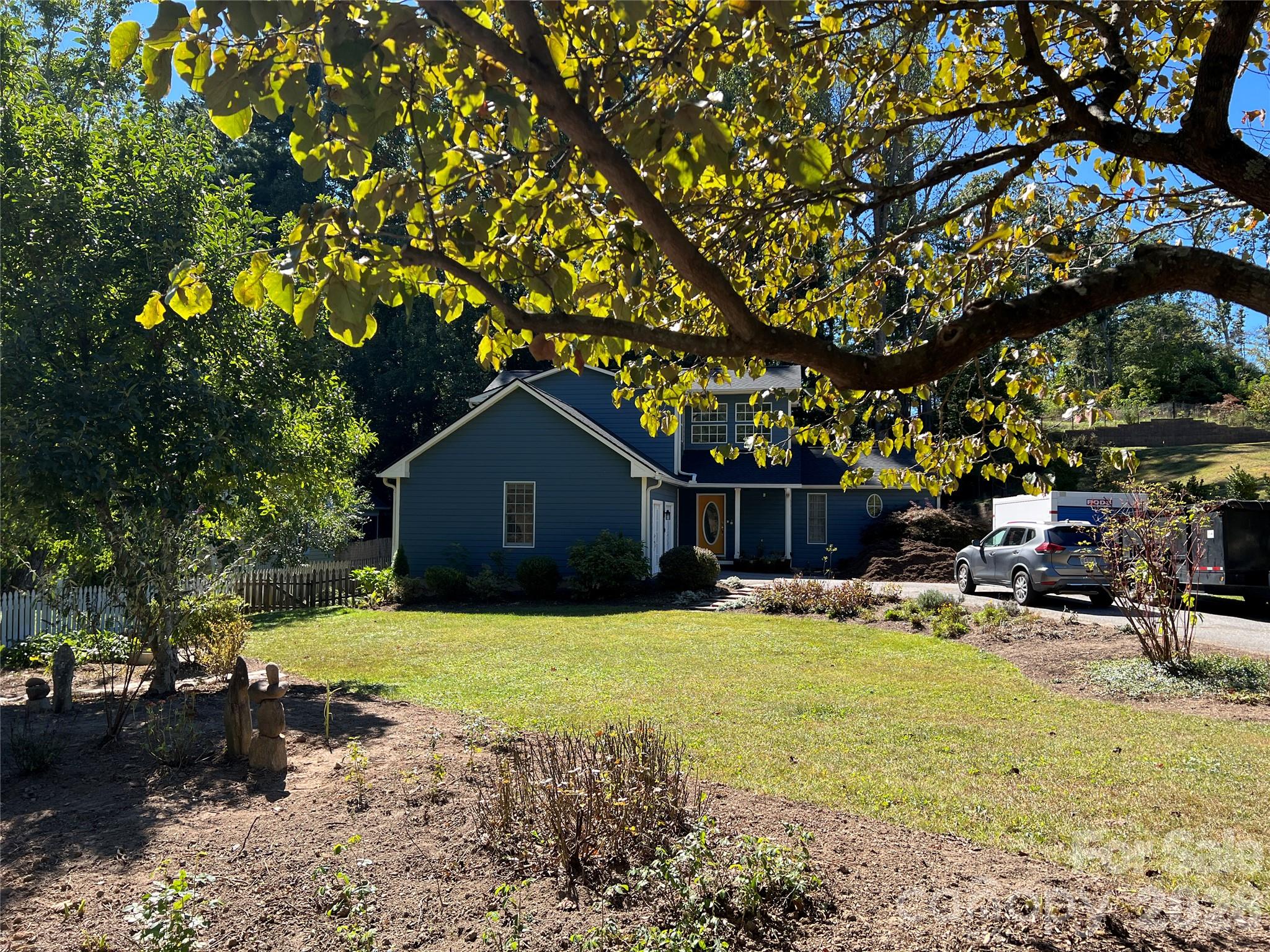 Blue two-story house with white trim, framed by a large tree with yellowing leaves.