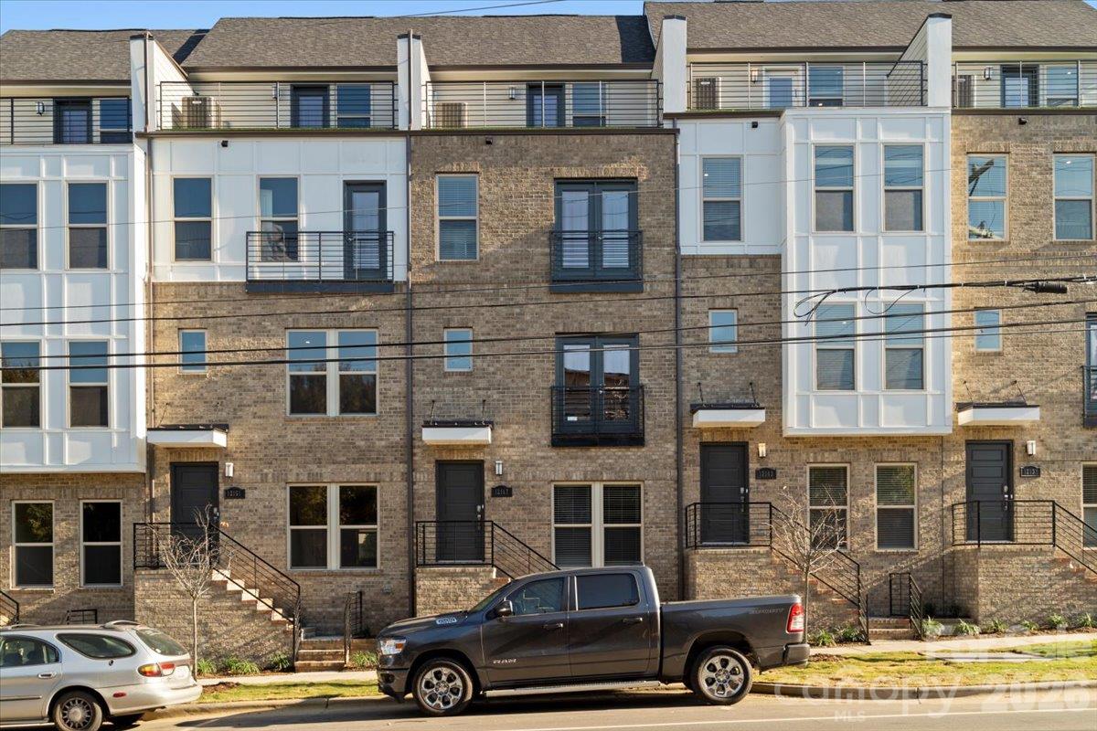Brick townhomes with white window bays, balconies, and parked vehicles along the street.
