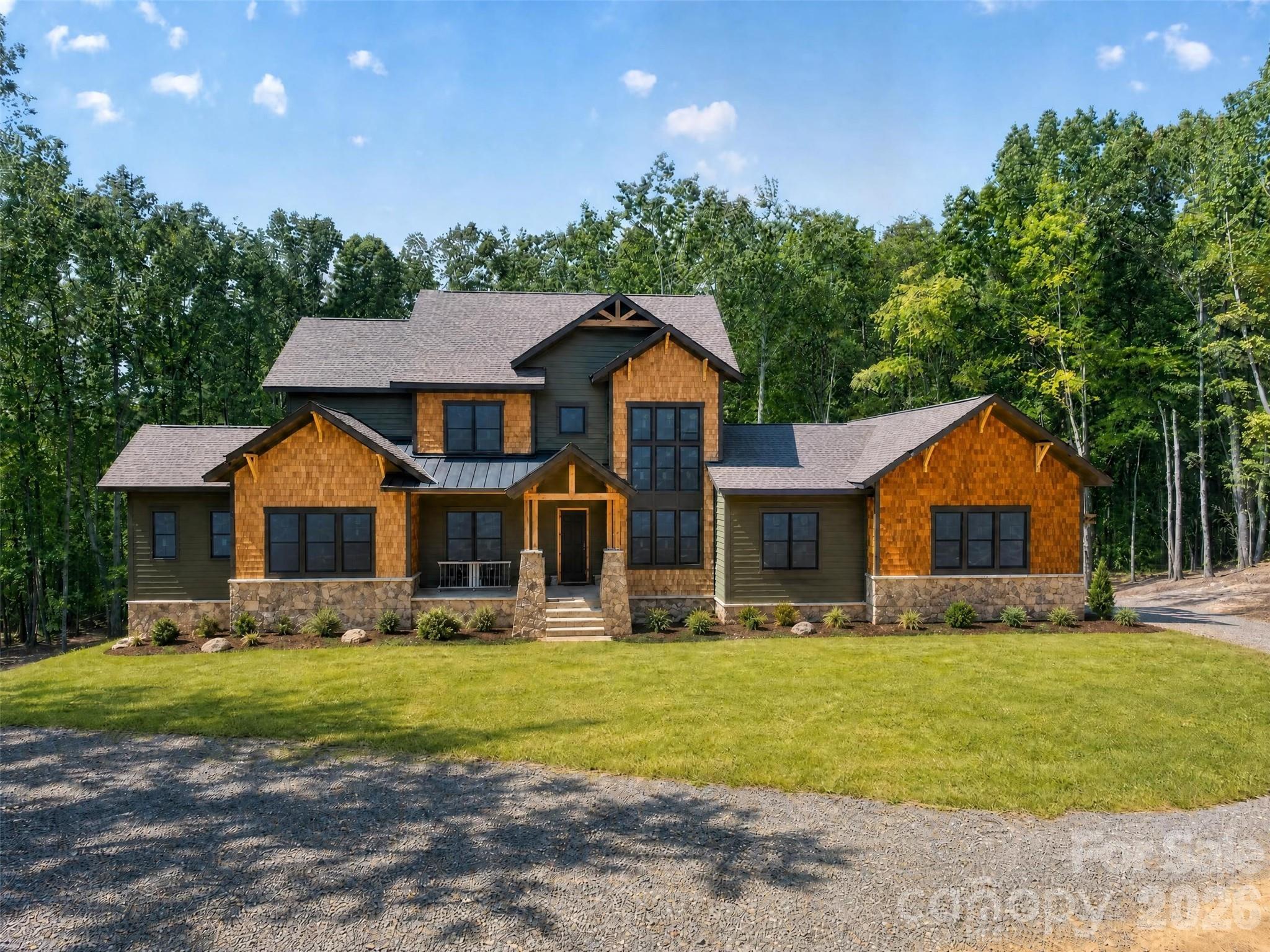 Two-story home with wood-shingle gables and stone accents, surrounded by trees.