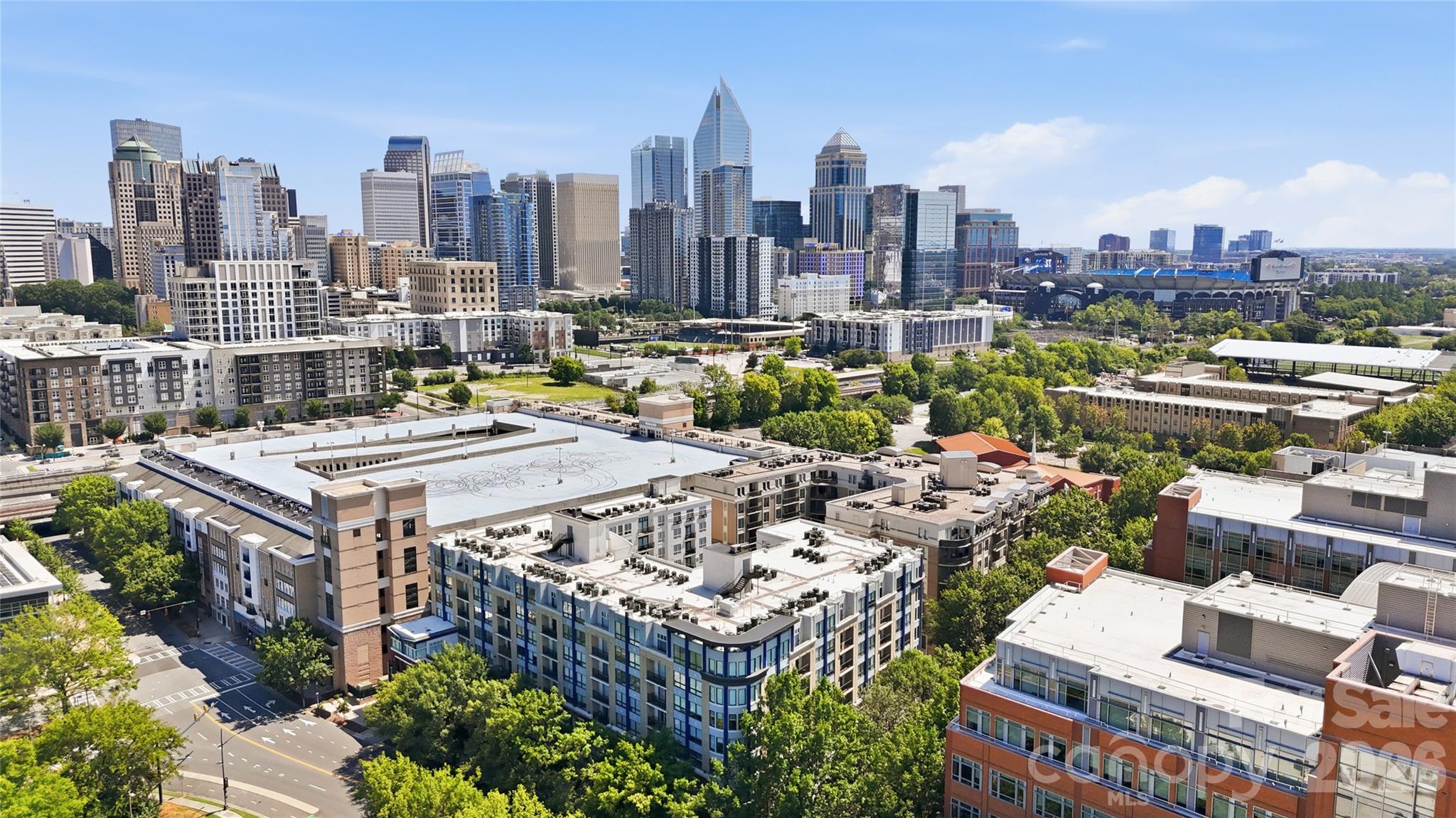Aerial panorama of downtown Charlotte, with high-rises and a stadium beneath a clear blue sky.
