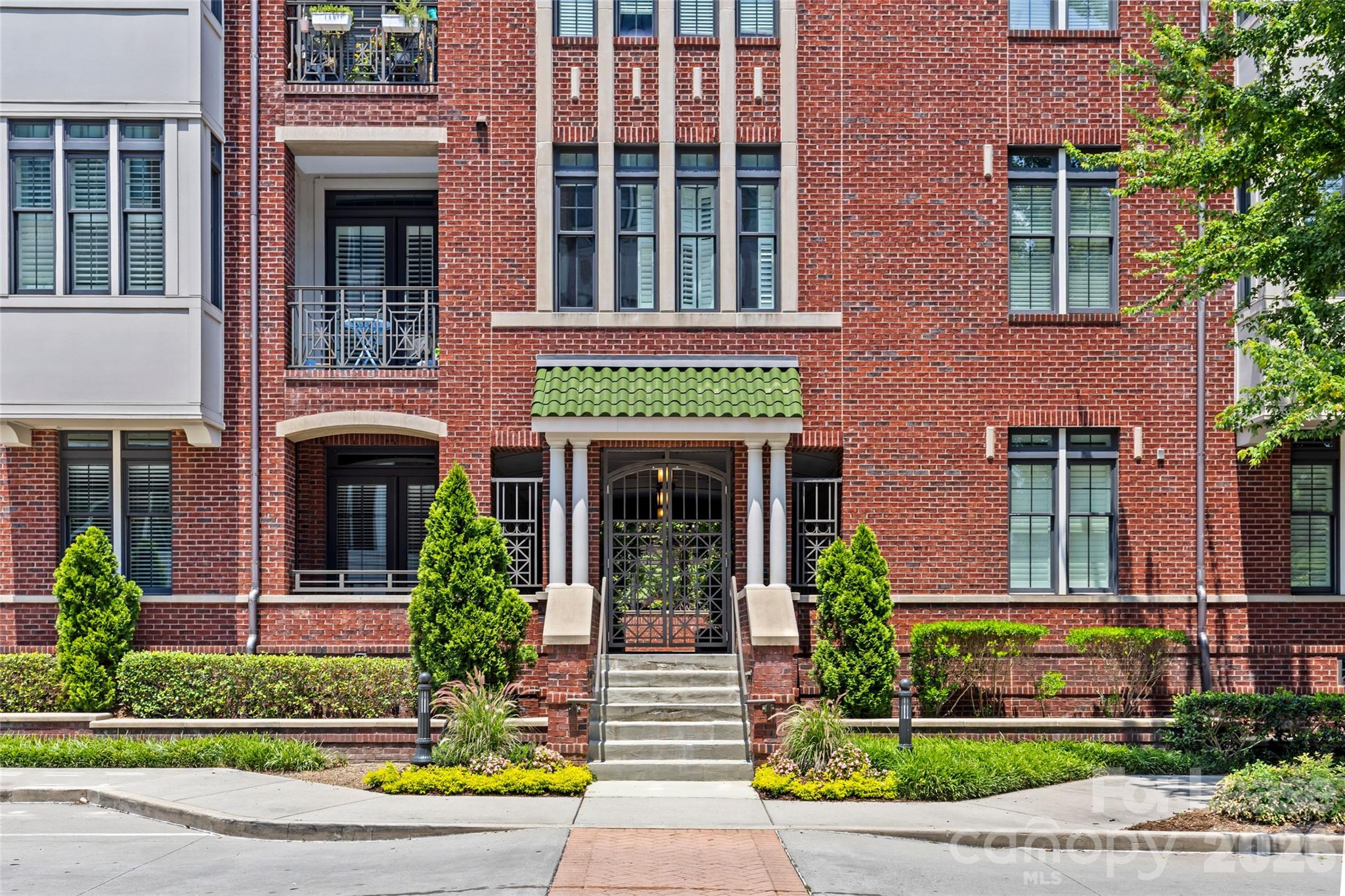 Brick condominium entrance with a green awning, balconies, and landscaped steps.
