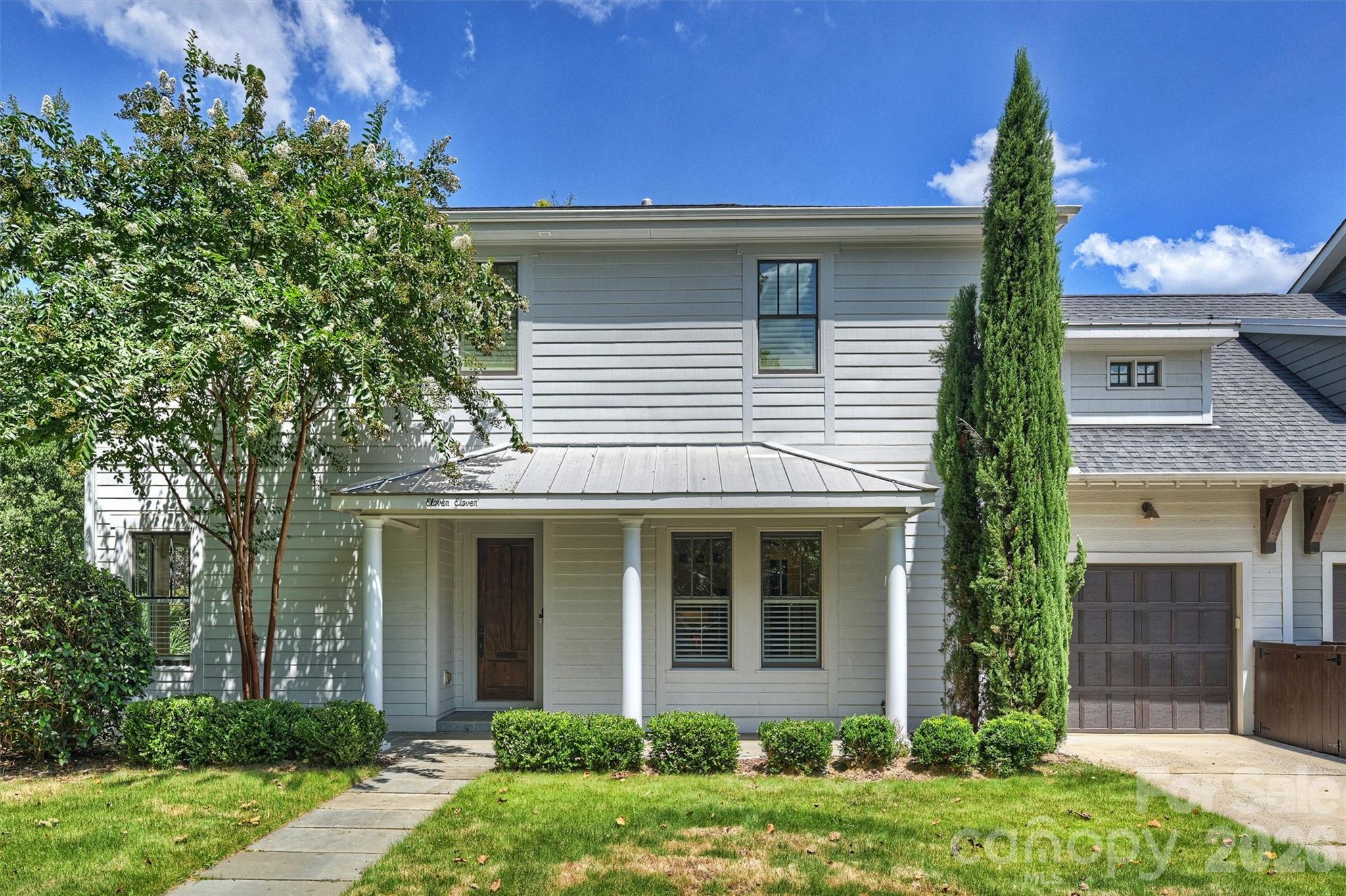 Two-story gray house with a covered porch, attached garage, and mature trees.