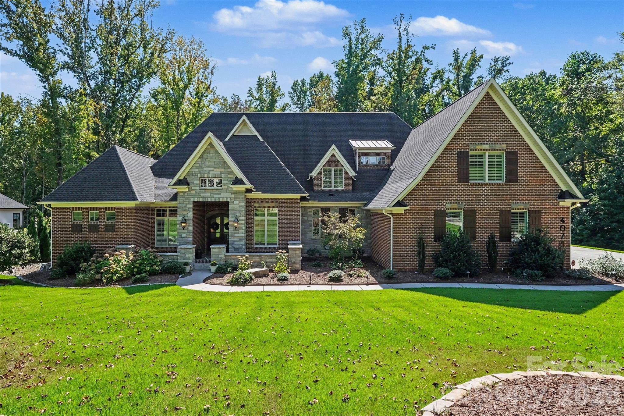 Two-story brick and stone house with multiple gables, landscaped beds, and a broad front lawn.