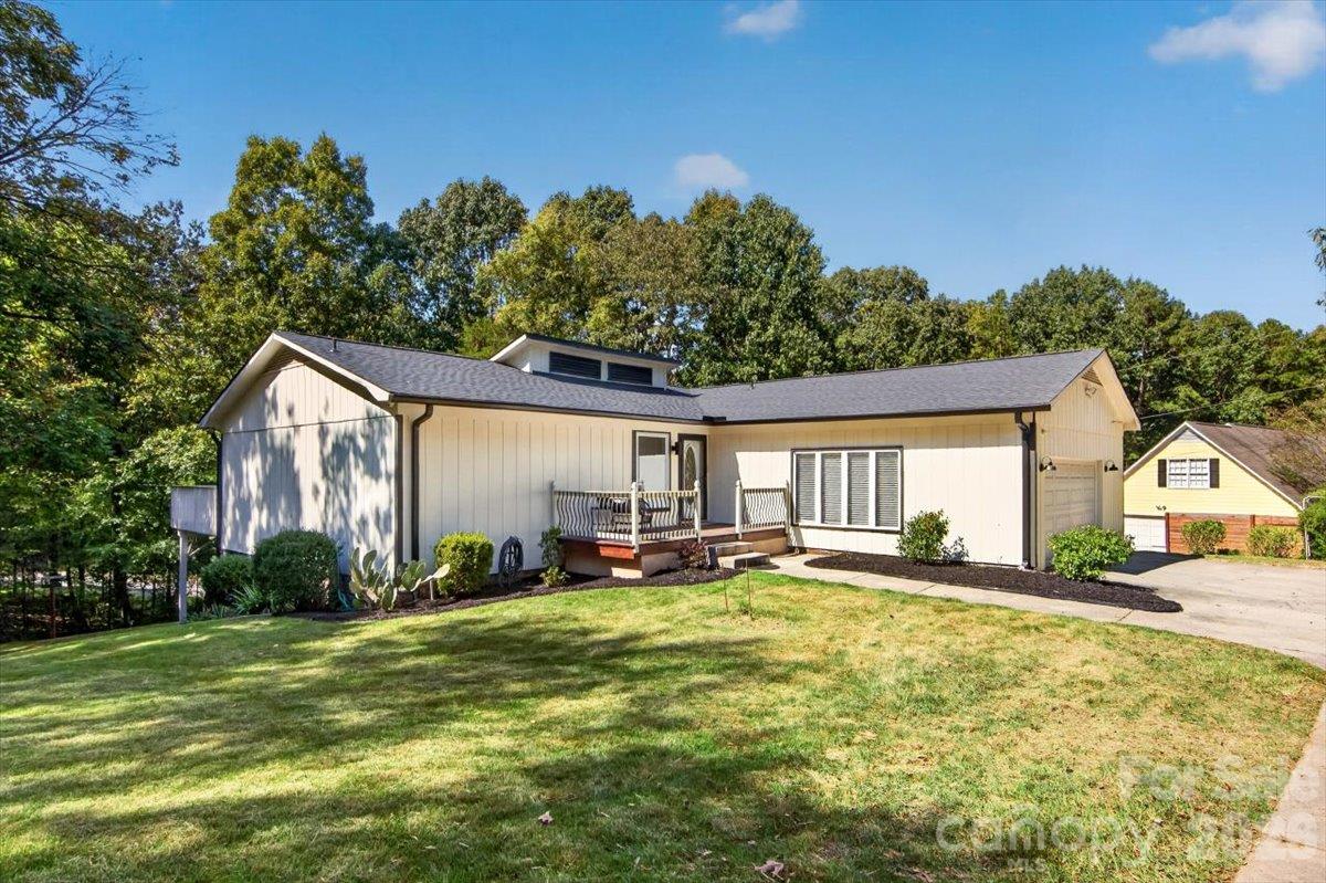 Single-story home with a small deck, attached garage, broad lawn, and mature trees.