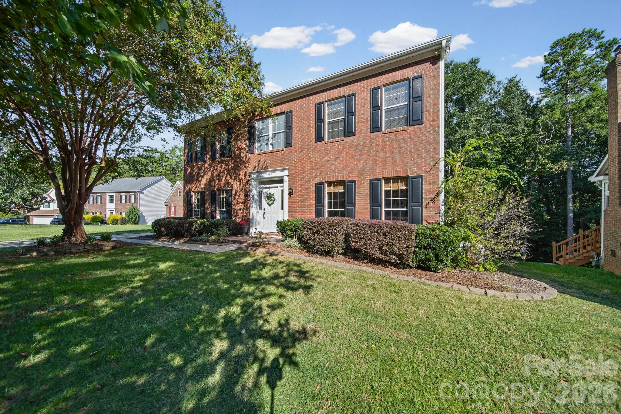 Two-story brick house with black shutters, a white front door, and a shaded lawn.