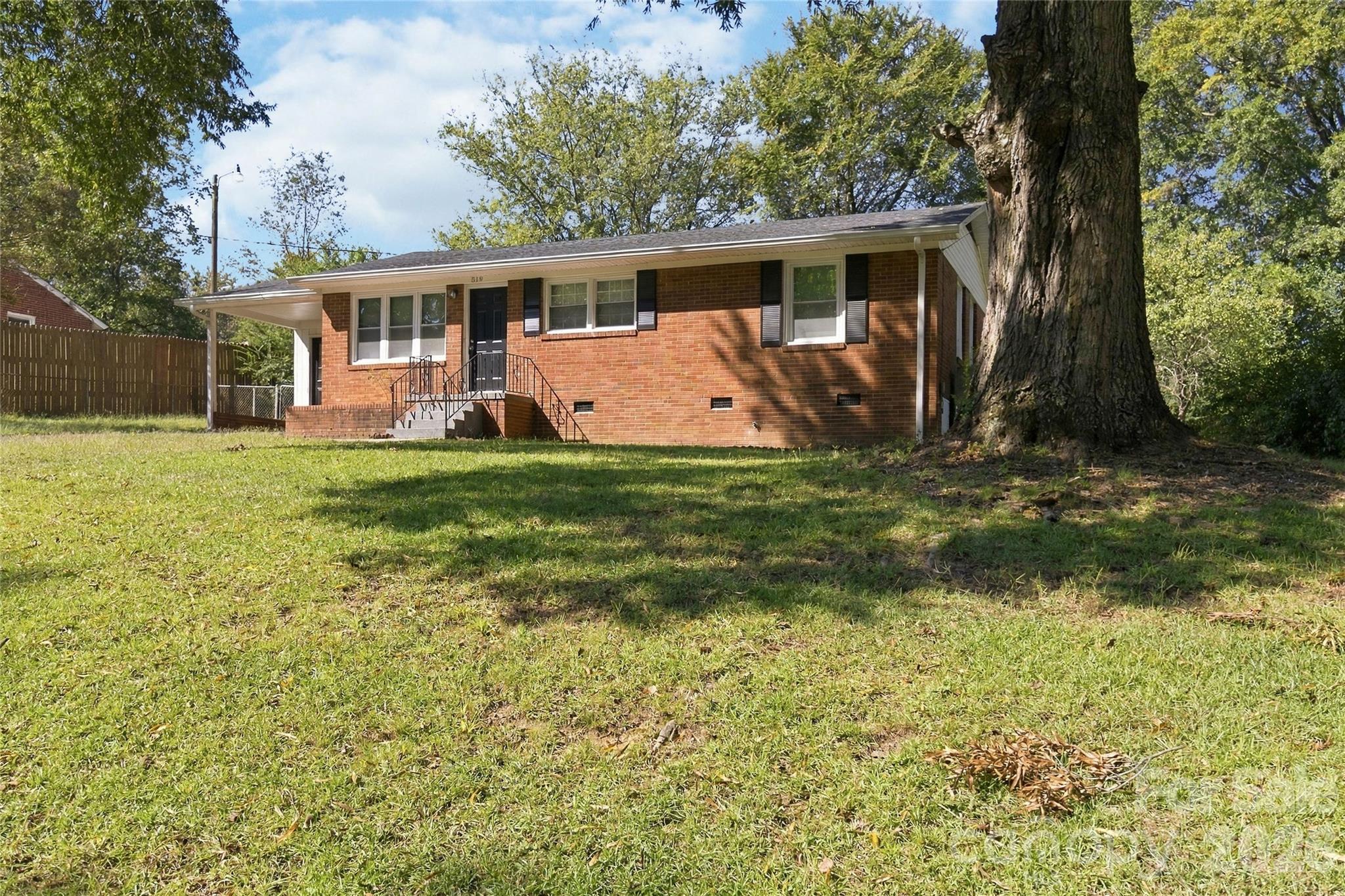 Red brick ranch house with a raised entry, broad lawn, and large mature tree in the foreground.