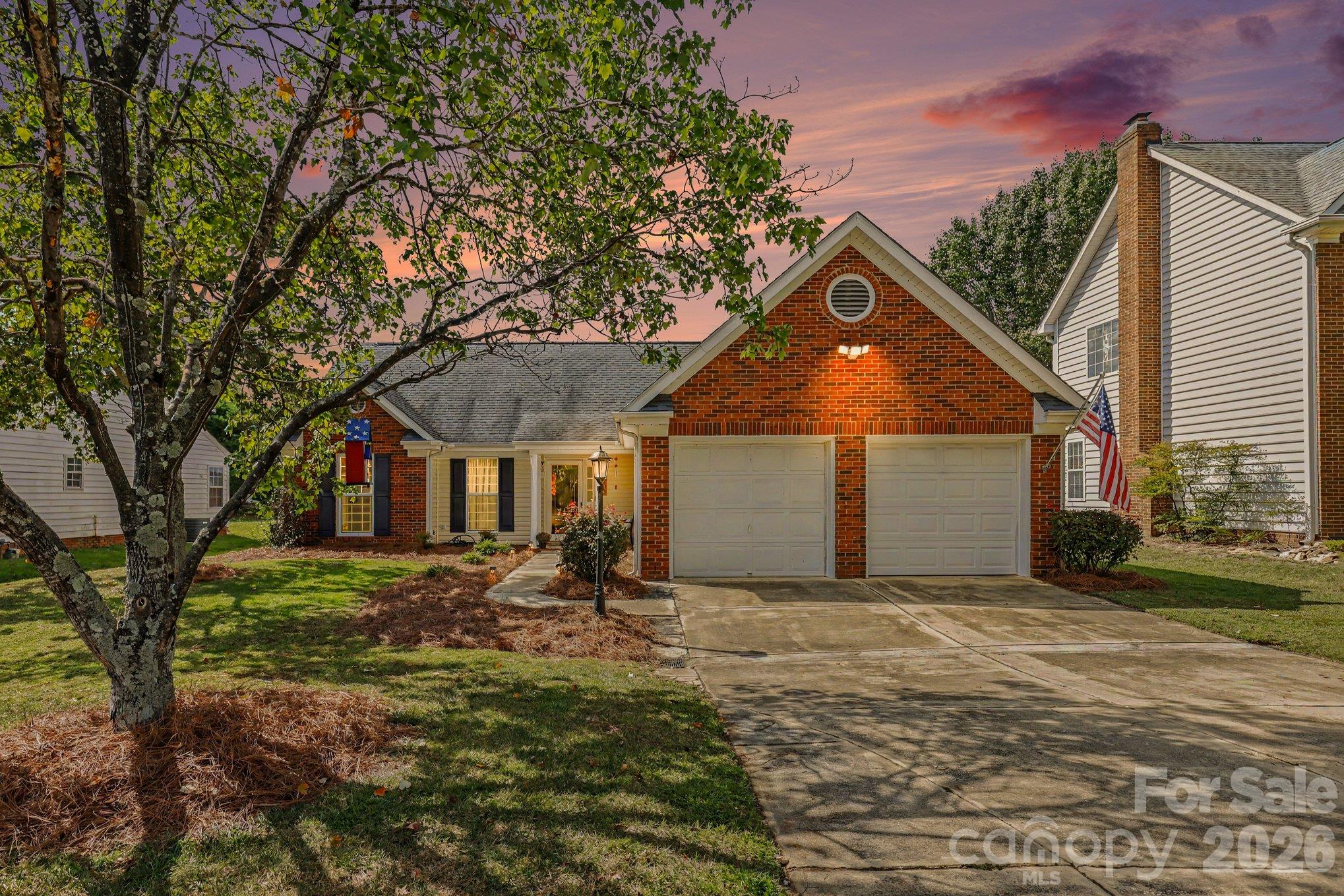 Brick home with two-car garage and American flag beneath a pink dusk sky.