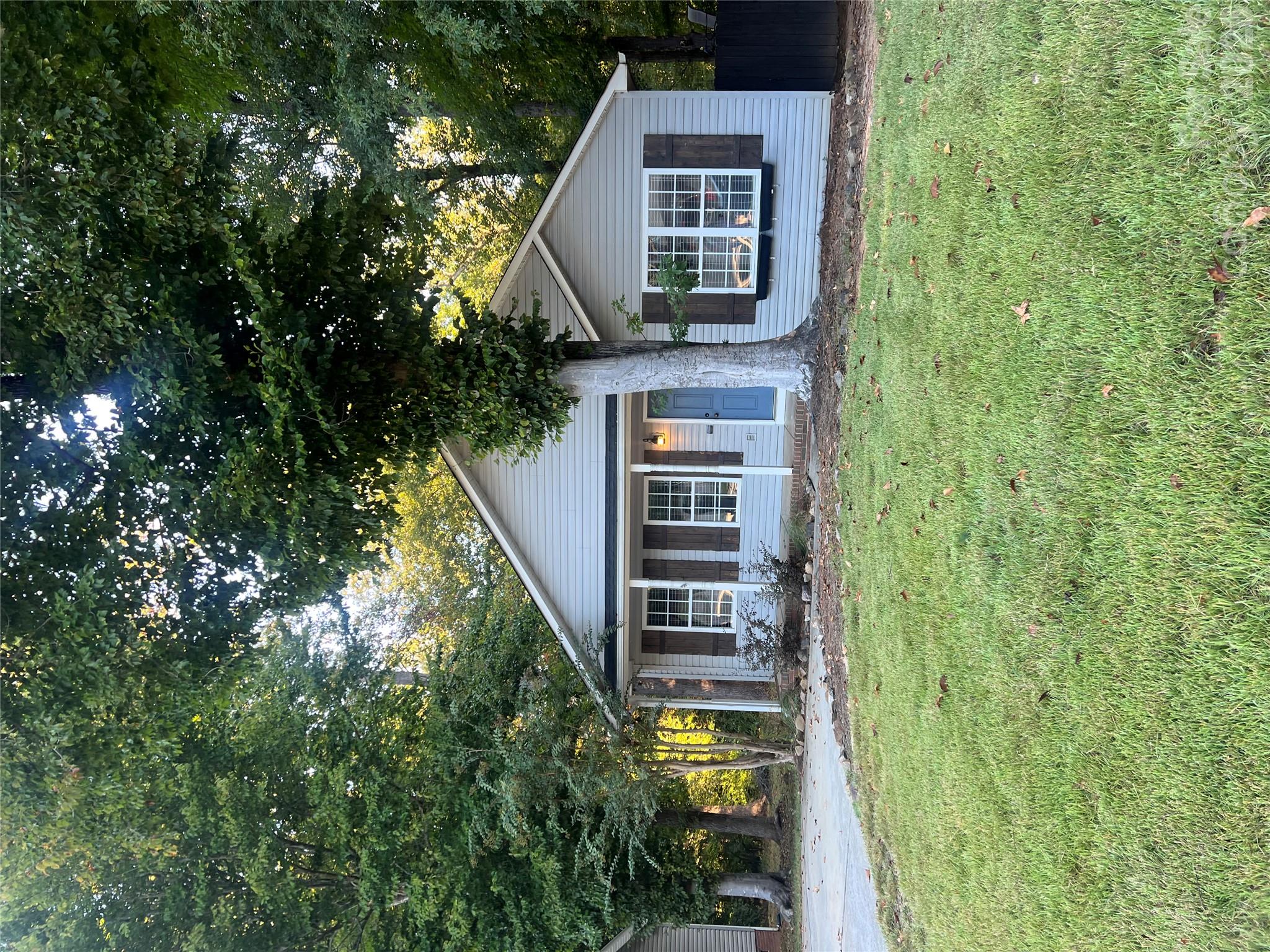 Gray single-story house with a blue front door, partly obscured by a large tree.