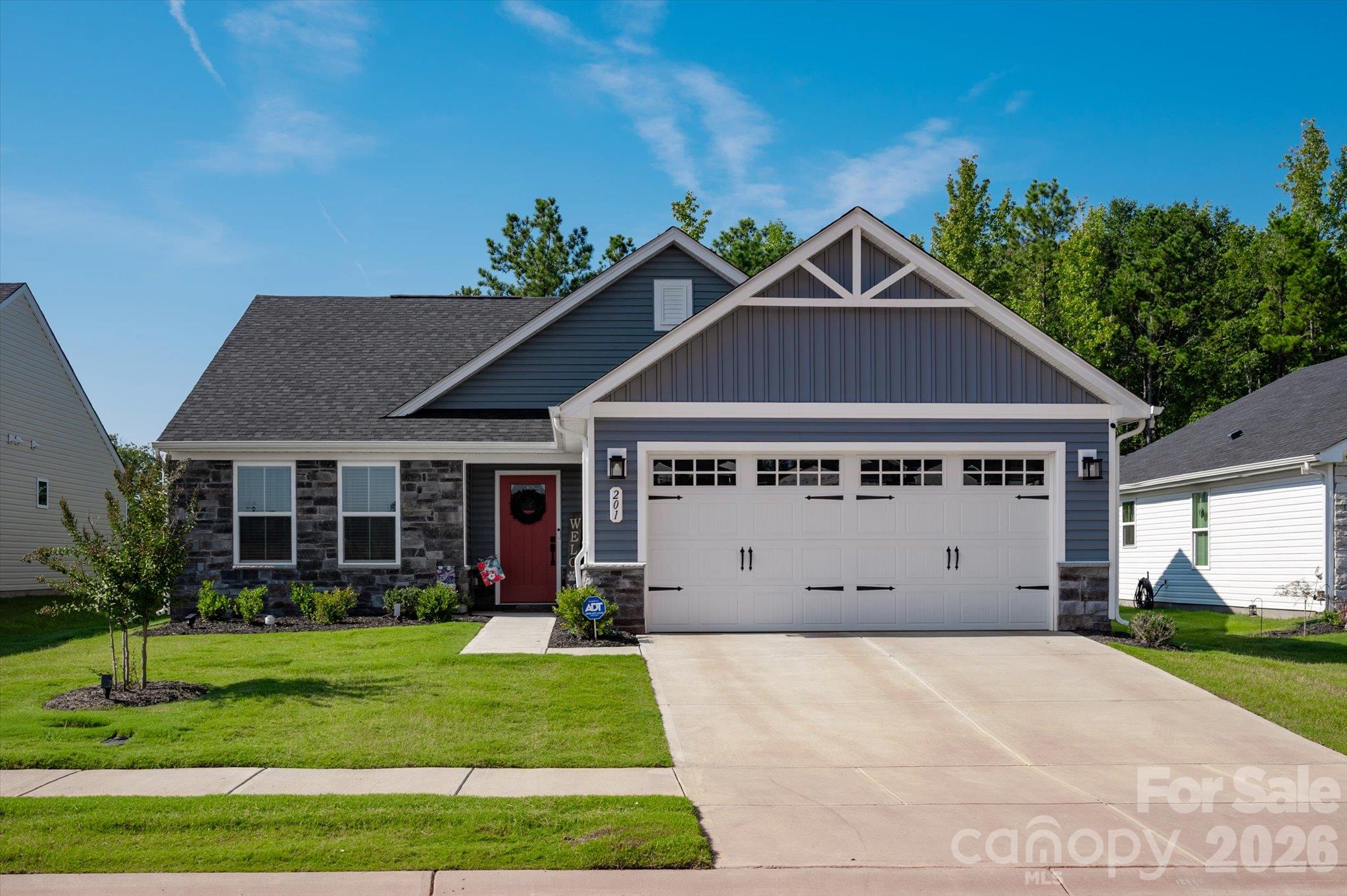 Blue-gray house with stone accents, a red front door, and a large white double garage.