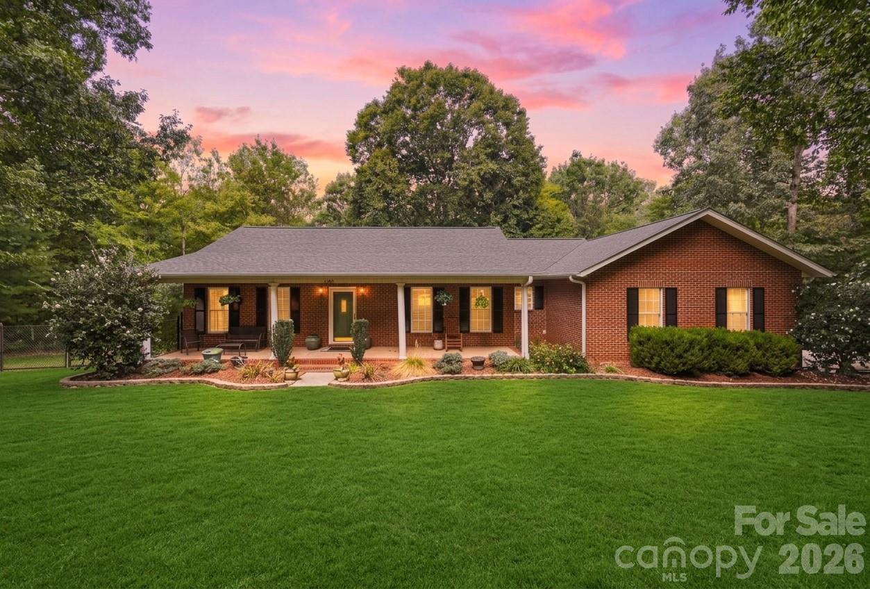 Red brick ranch house with a covered porch and broad lawn beneath a pink dusk sky.