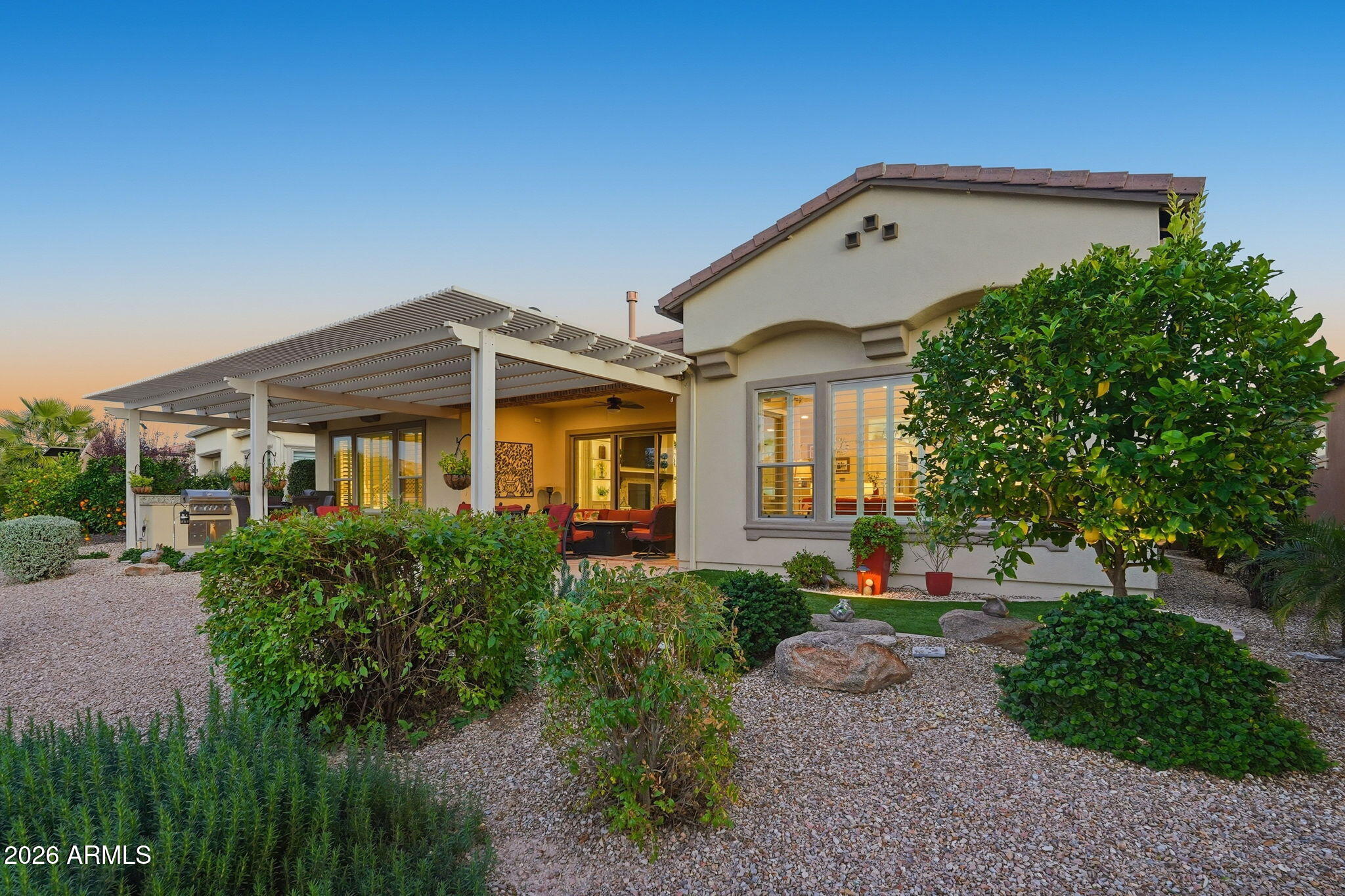 Home’s rear exterior with a pergola-covered patio and landscaped gravel yard at sunset.