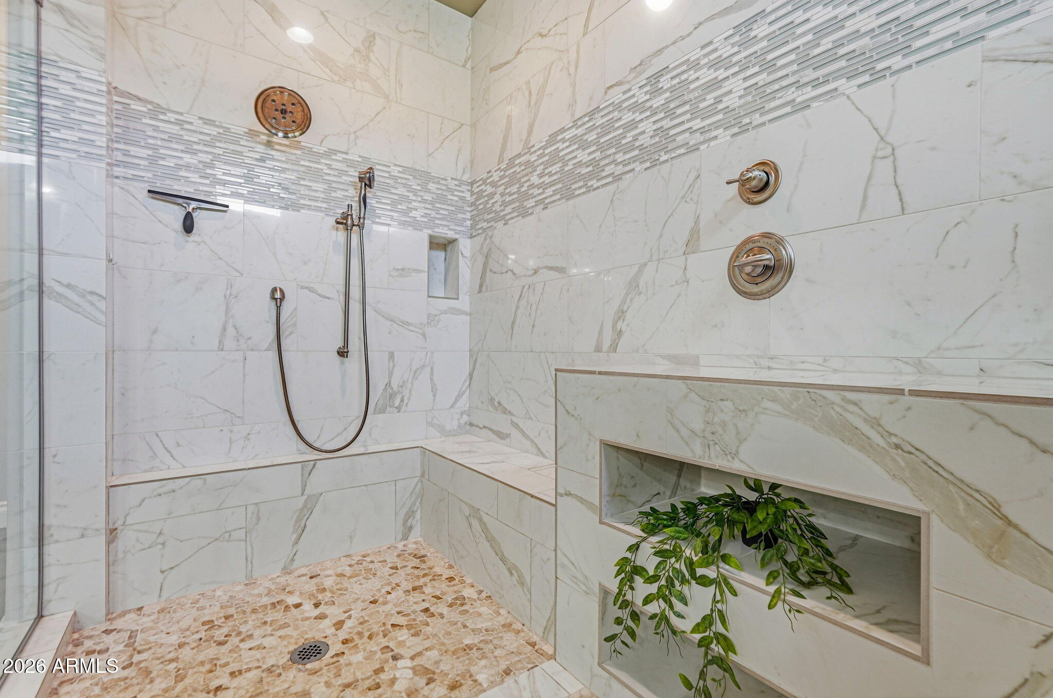 Walk-in shower with marble-look tile, bronze fixtures, a built-in bench, and a pebble mosaic floor.