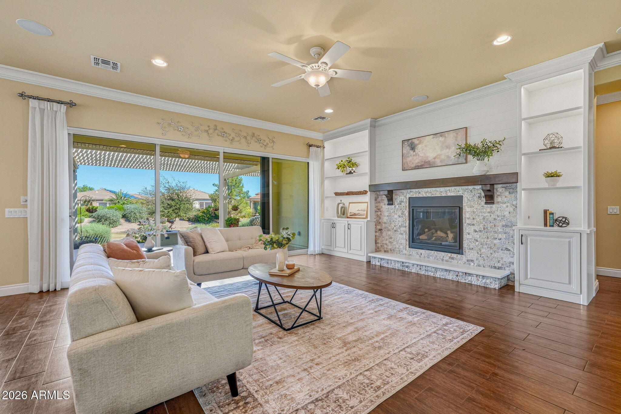 Staged living room with a stone fireplace, built-in shelving, and sliding doors opening to a landscaped backyard.