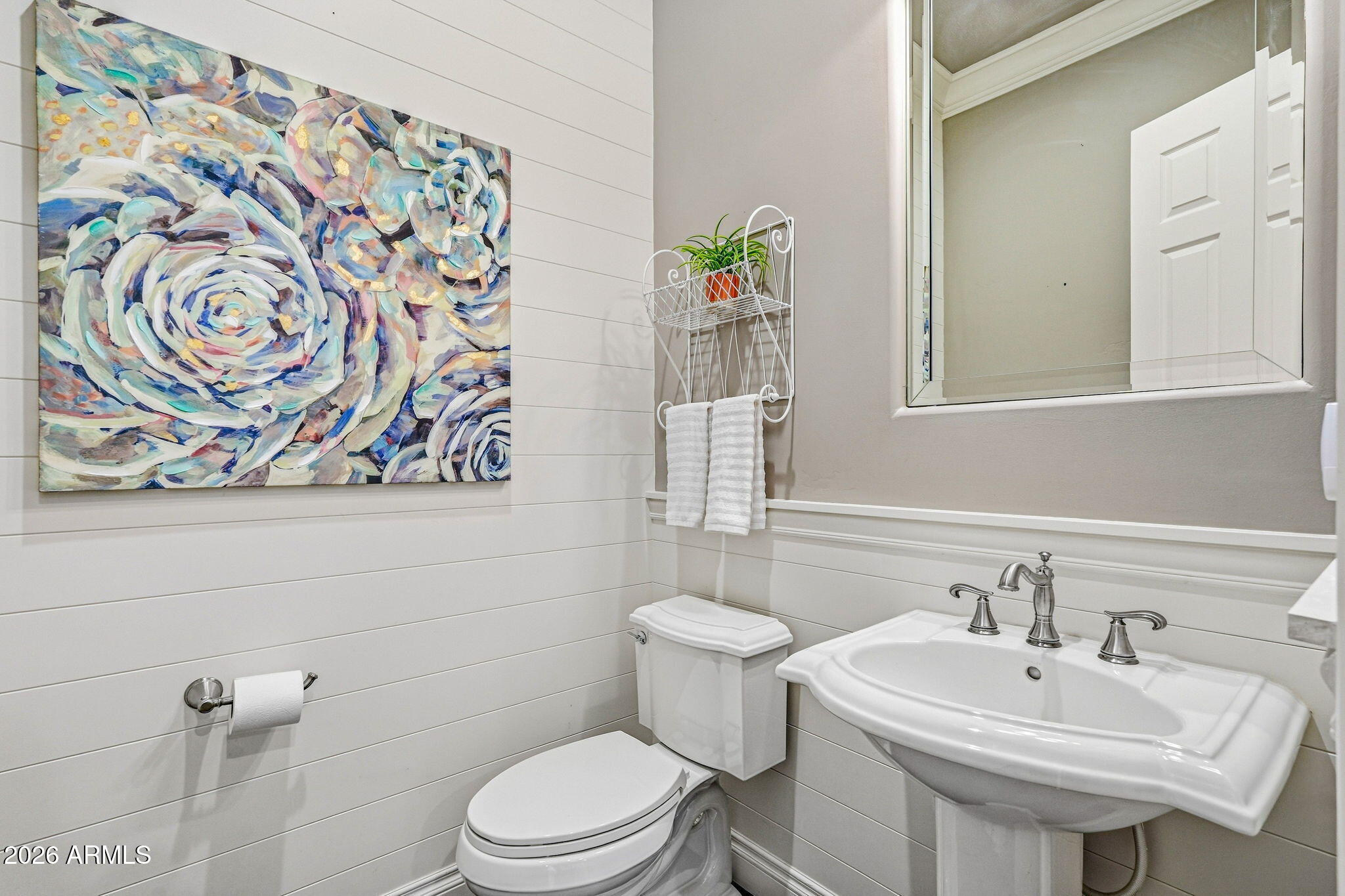 Bathroom with a pedestal sink, white paneled walls, and large colorful floral artwork.
