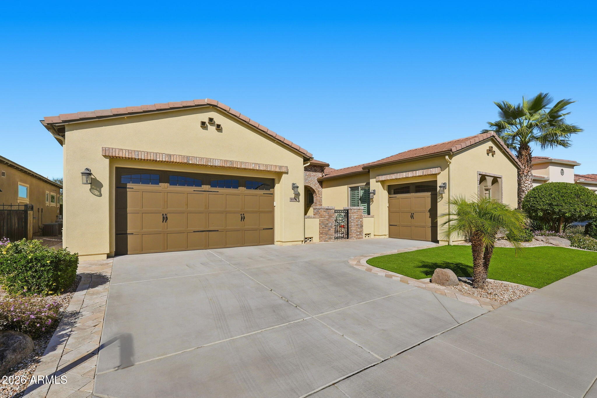 Beige stucco home with two brown garage doors, wide driveway, palm trees, and a green front lawn.