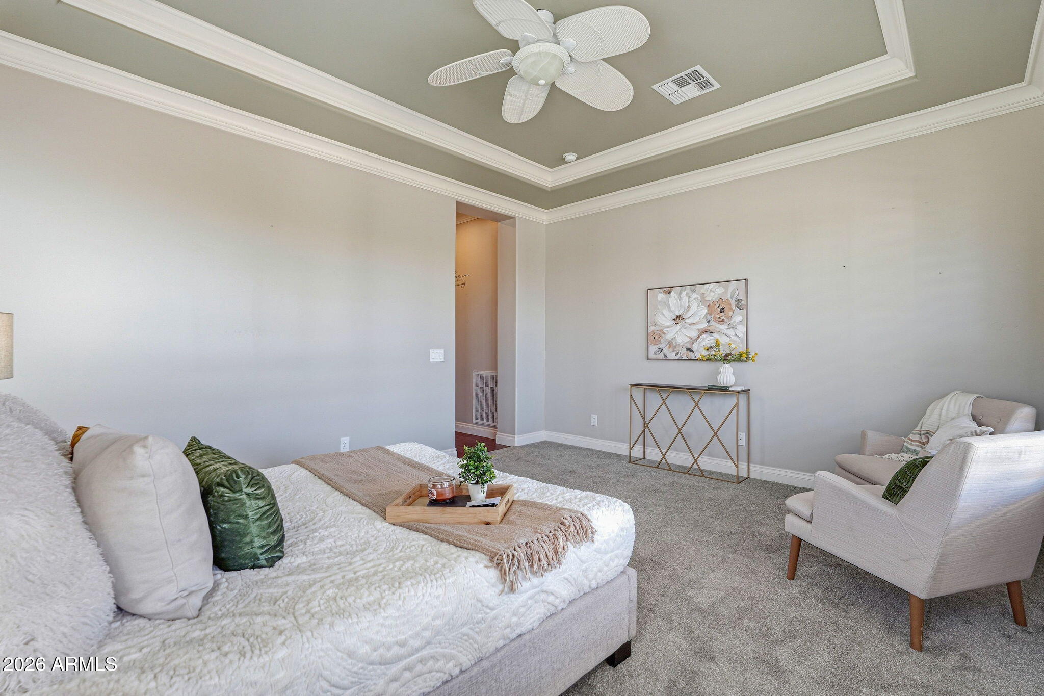 Staged bedroom with a tray ceiling, ceiling fan, and upholstered seating.