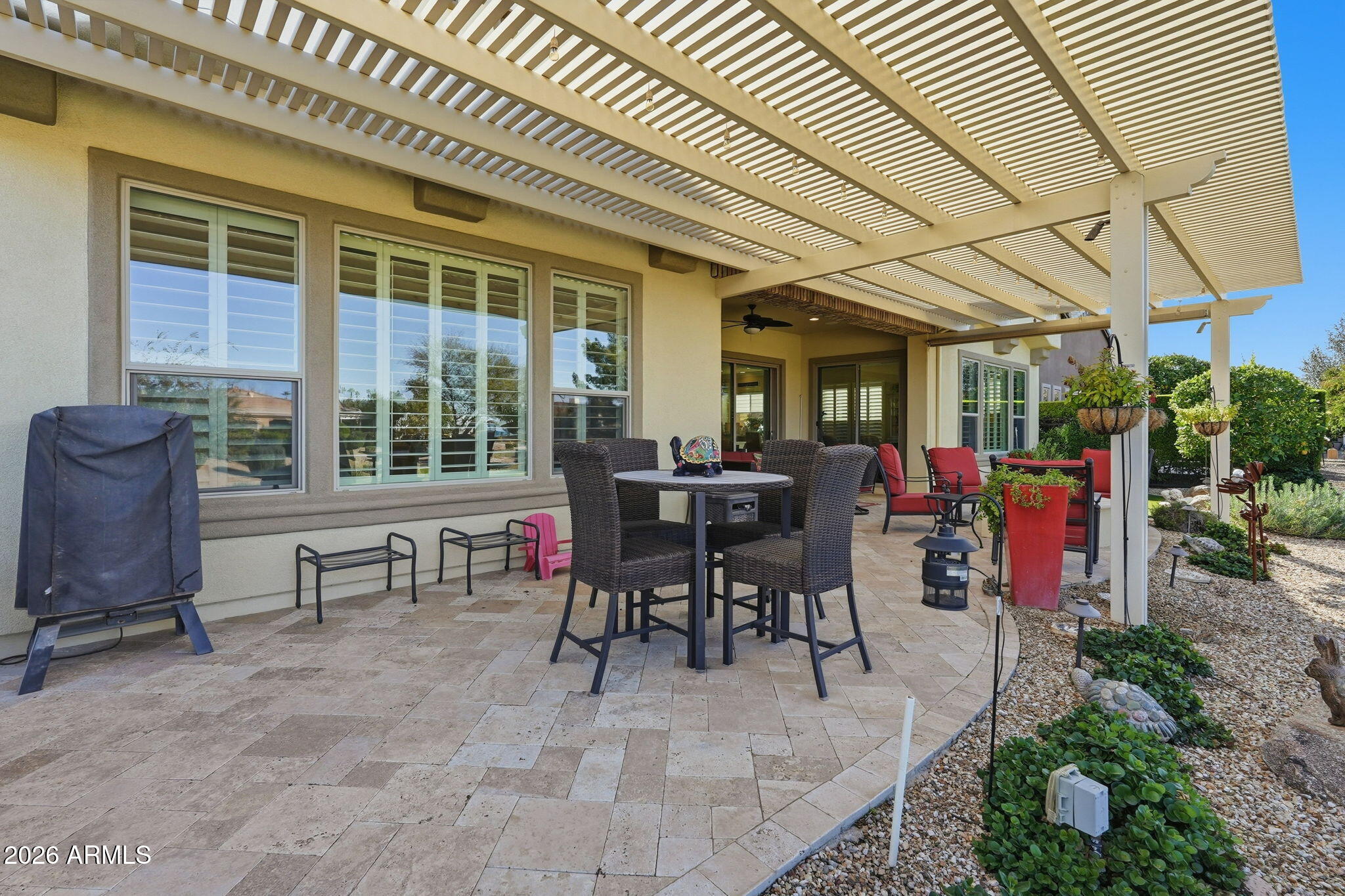 Back patio beneath a large pergola, furnished with wicker dining chairs and red outdoor seating.