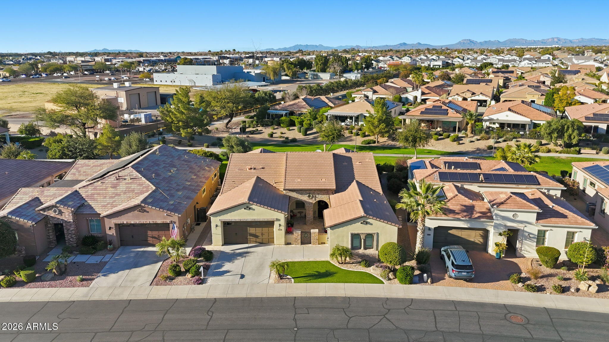 Aerial view of a Queen Creek home and neighborhood, with solar panels on nearby roofs and mountains in the distance.