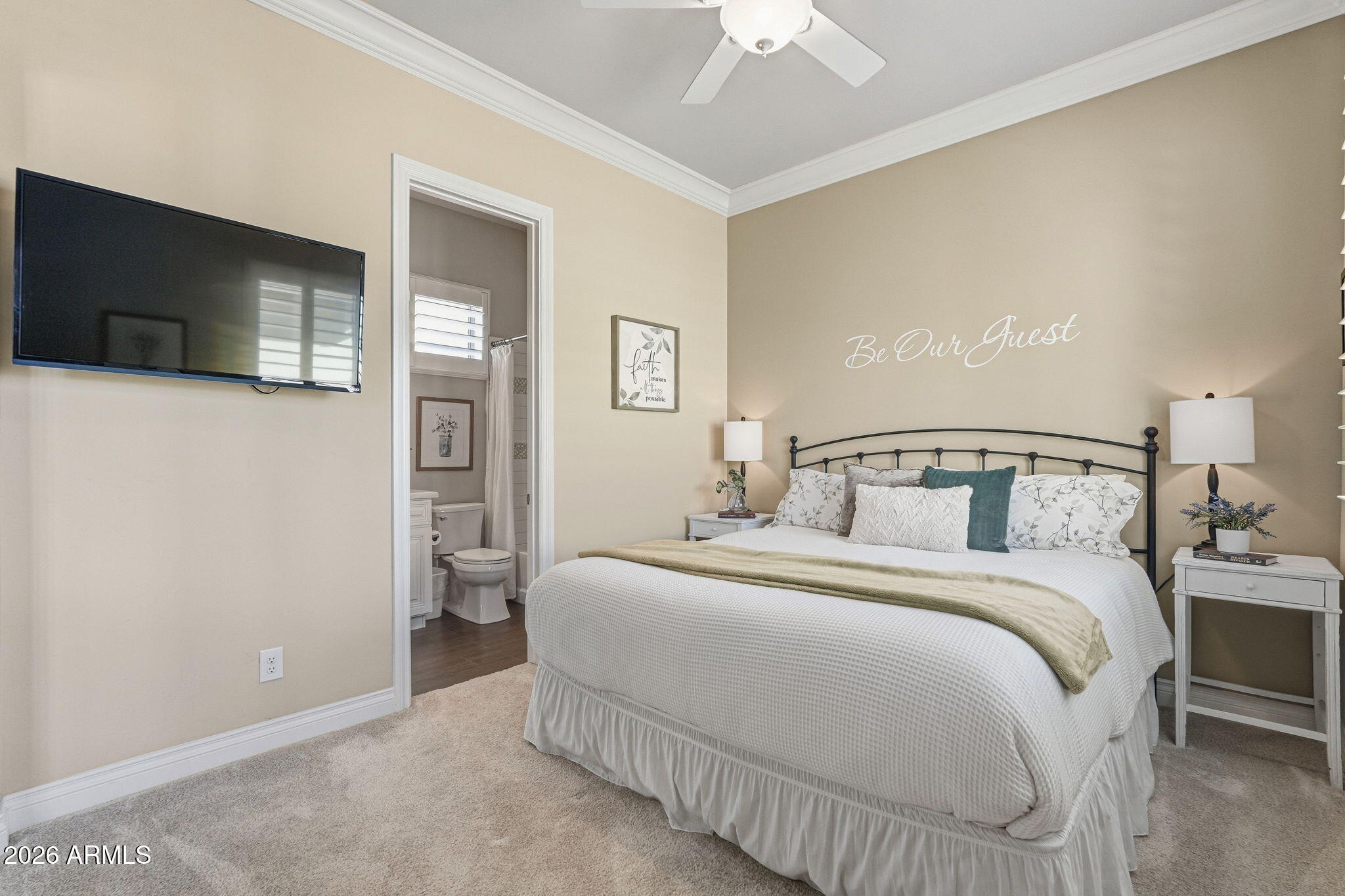 Guest bedroom with a large white bed, black metal headboard, and en-suite bathroom doorway.