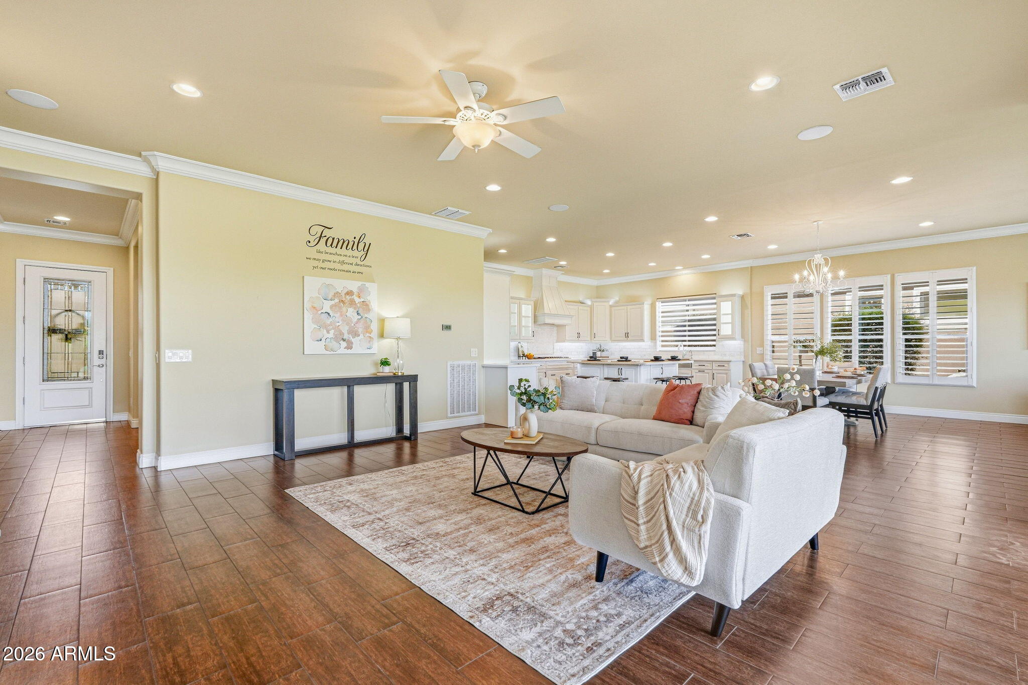 Open-plan living room with a large light sectional, tiled floors, and a bright white kitchen beyond.