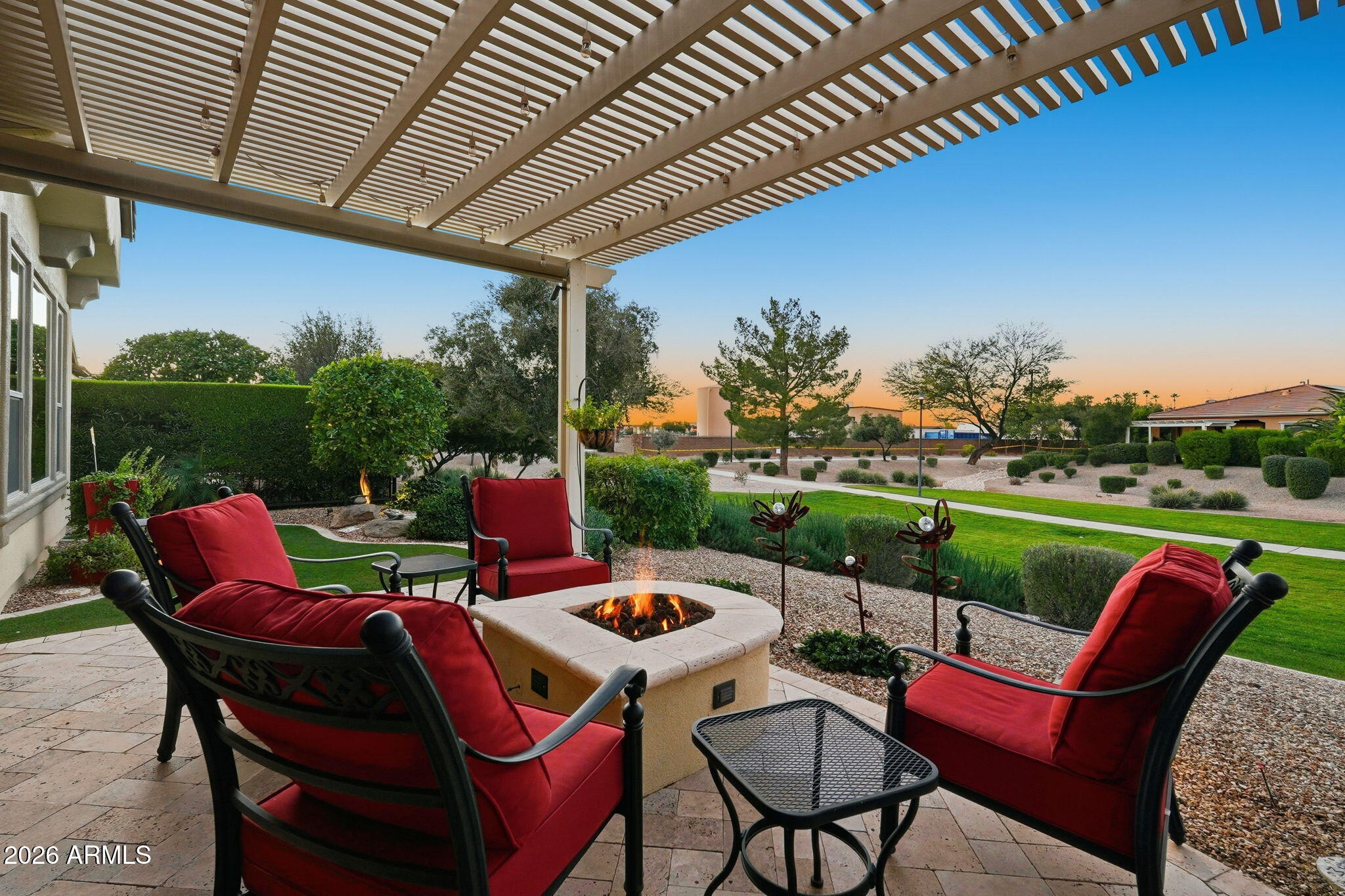 Covered patio with red lounge chairs around a fire pit, overlooking a landscaped yard at sunset.
