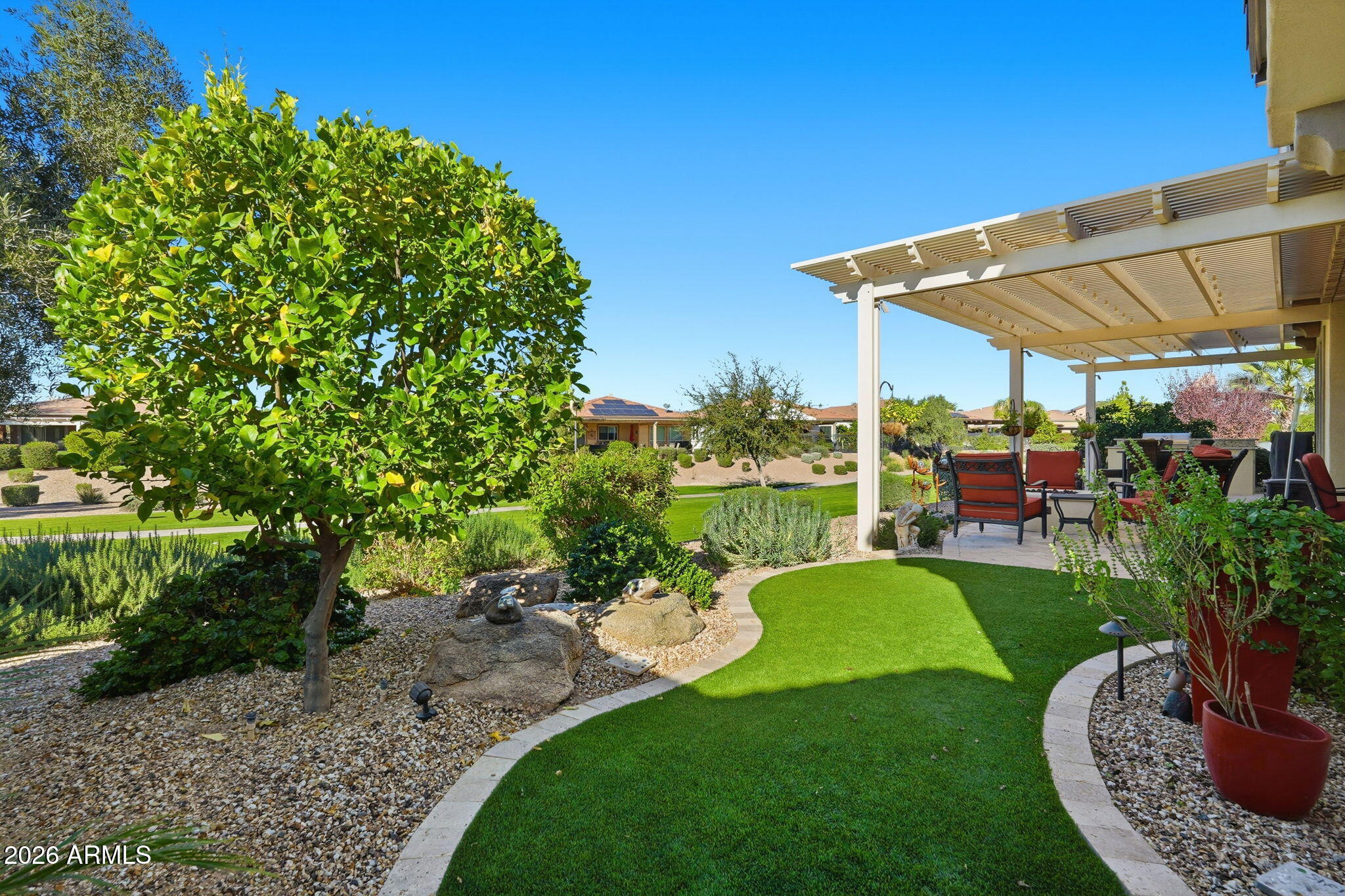 Backyard patio with pergola seating, curved green lawn, gravel landscaping, and a mature tree.