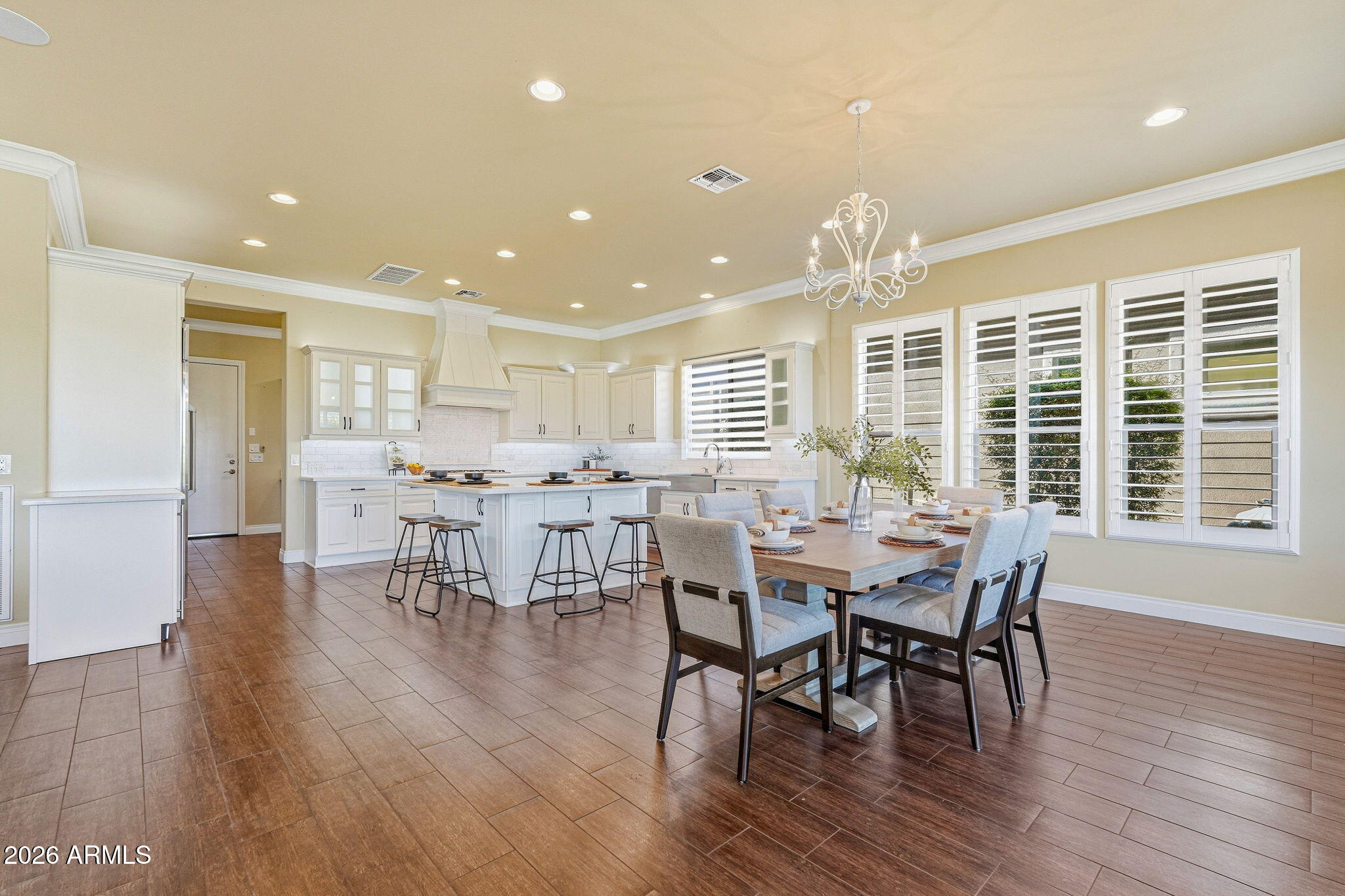 Bright kitchen and dining area with a white island, set table, brown tile floors, and plantation shutters.