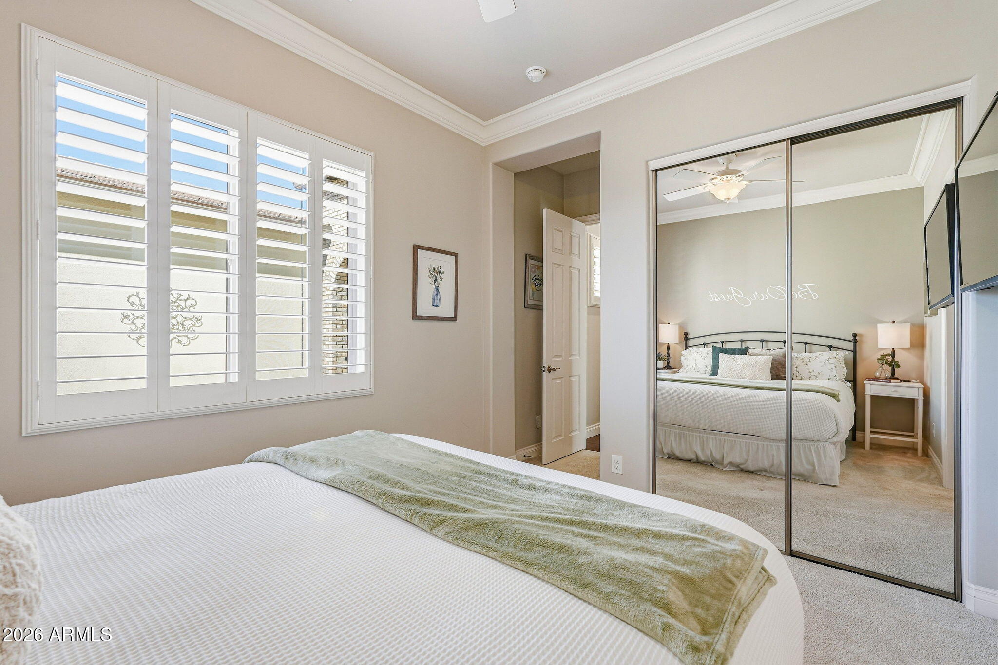 Bedroom with plantation shutters and mirrored closet doors reflecting a neatly made bed.