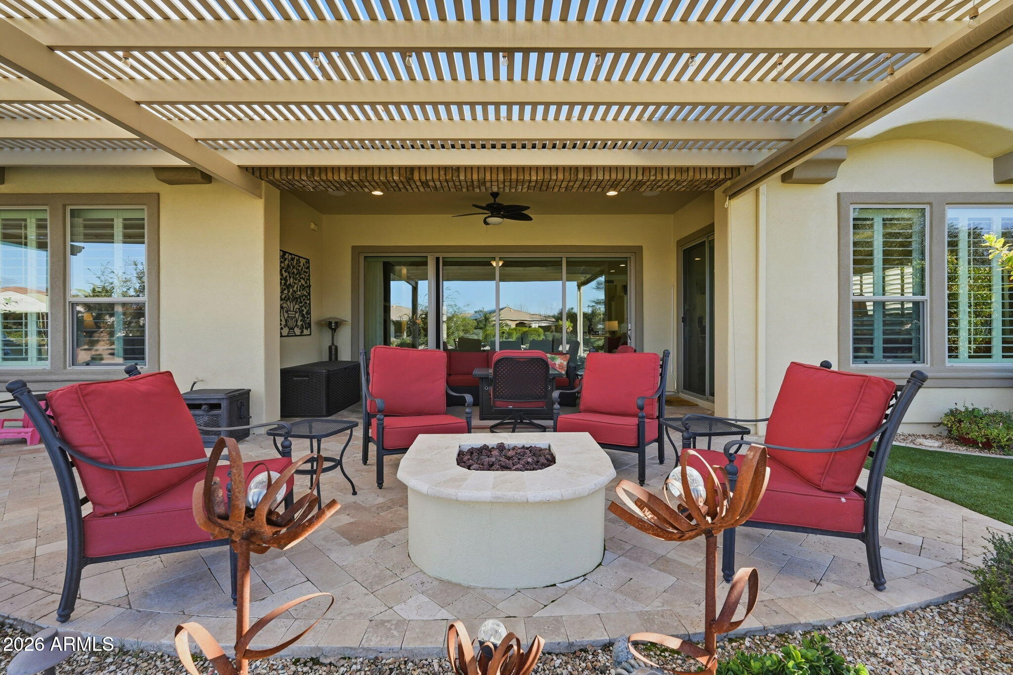 Covered patio with red-cushioned seating, a stone fire pit, and a slatted pergola.