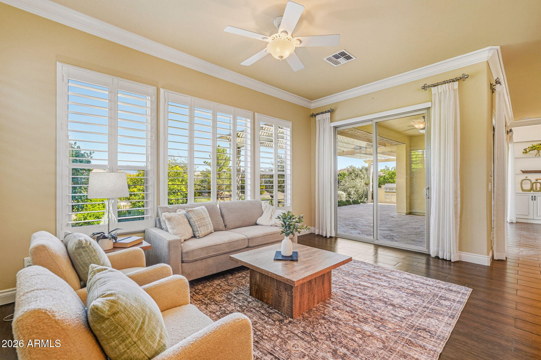 Furnished living room with plantation shutters, beige seating, and sliding glass doors to a covered patio.