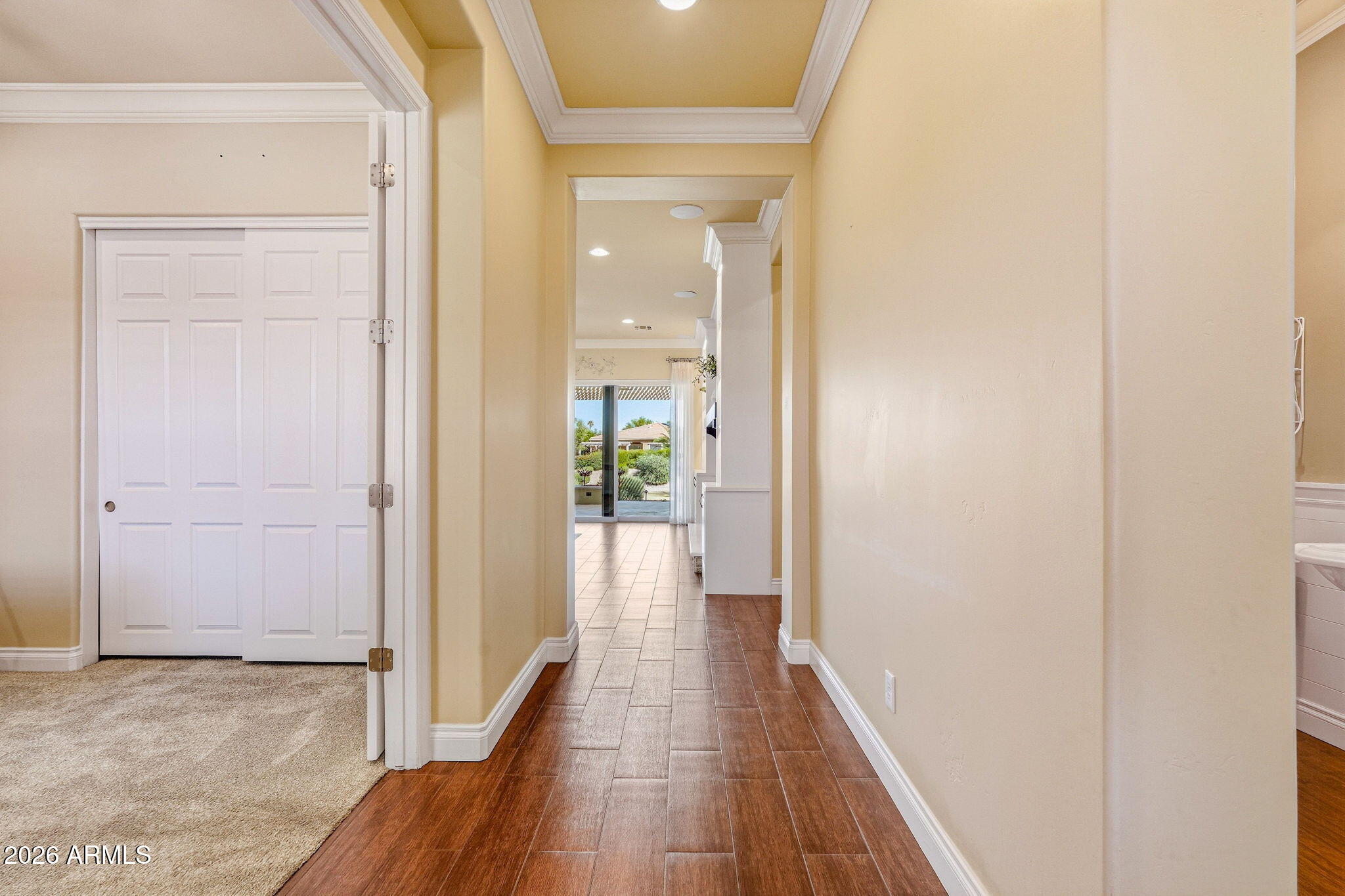 Hallway with wood-look tile, white trim, and a view through to sliding glass doors.