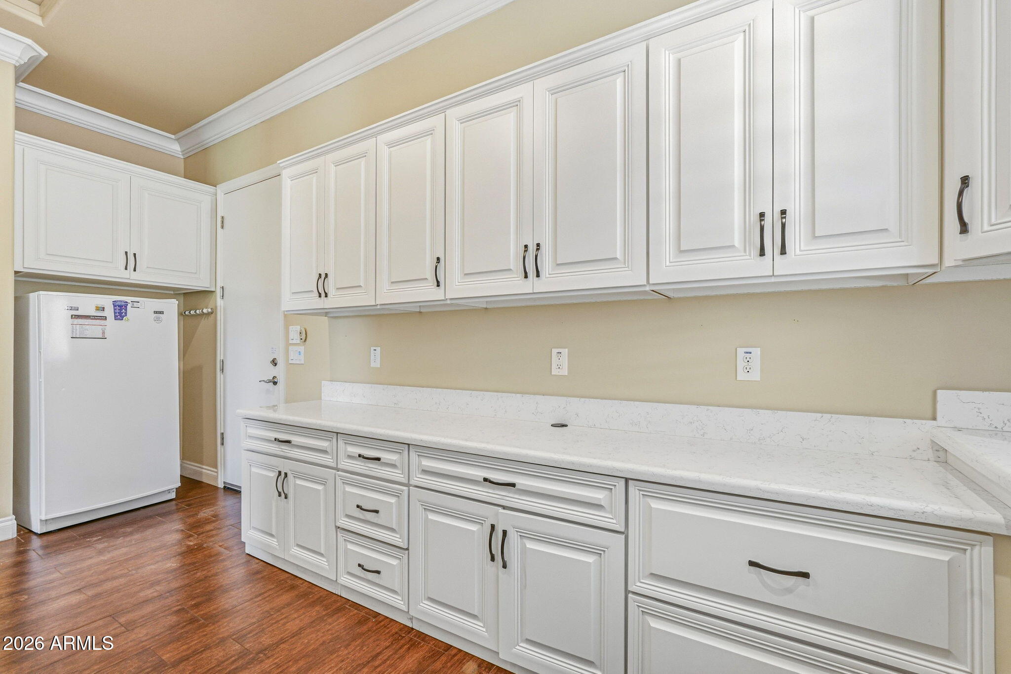 Kitchen with white cabinets and counters, a refrigerator, and dark wood flooring.