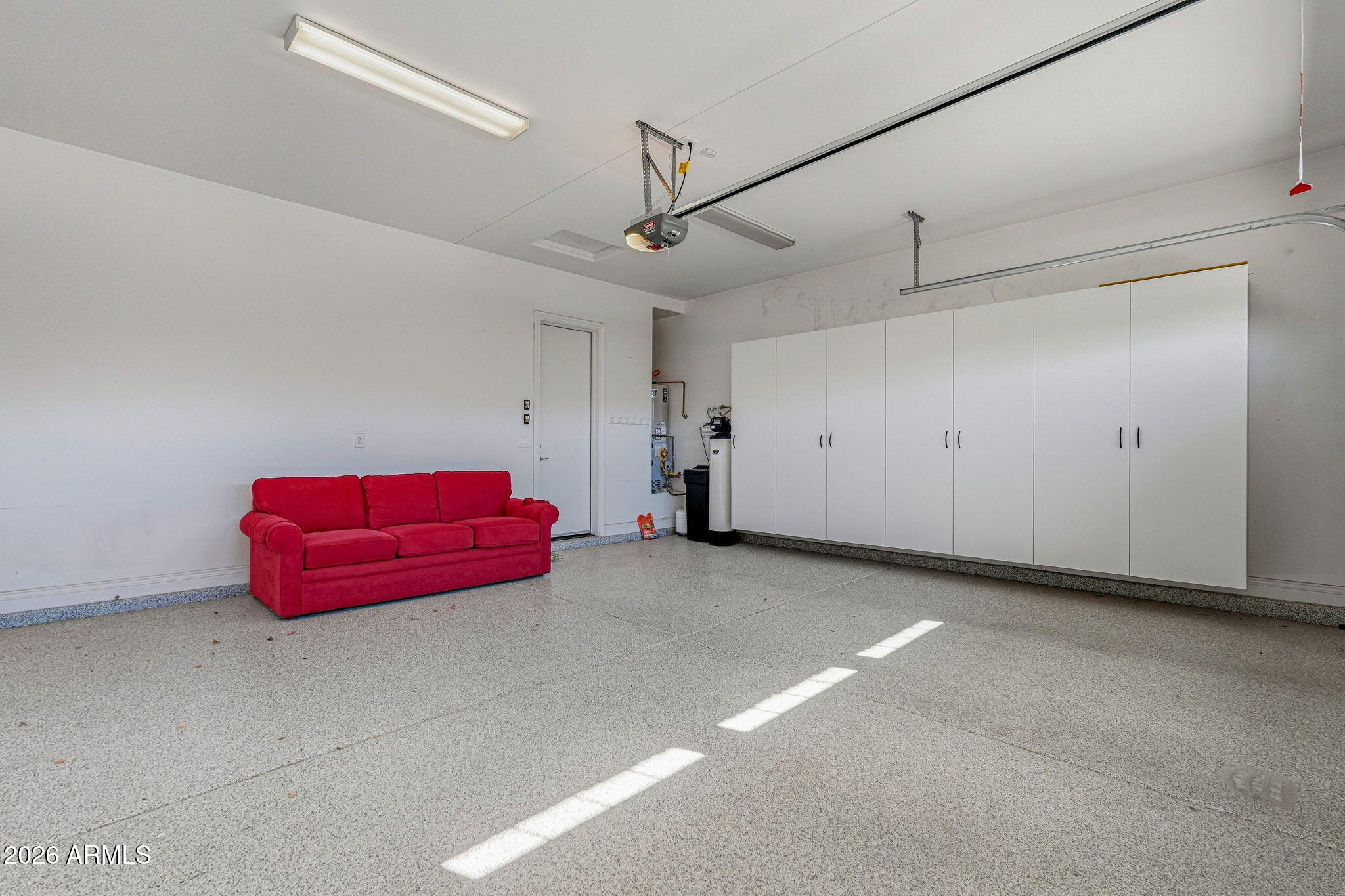 Garage with white storage cabinets, a red sofa, and sunlight across the concrete floor.