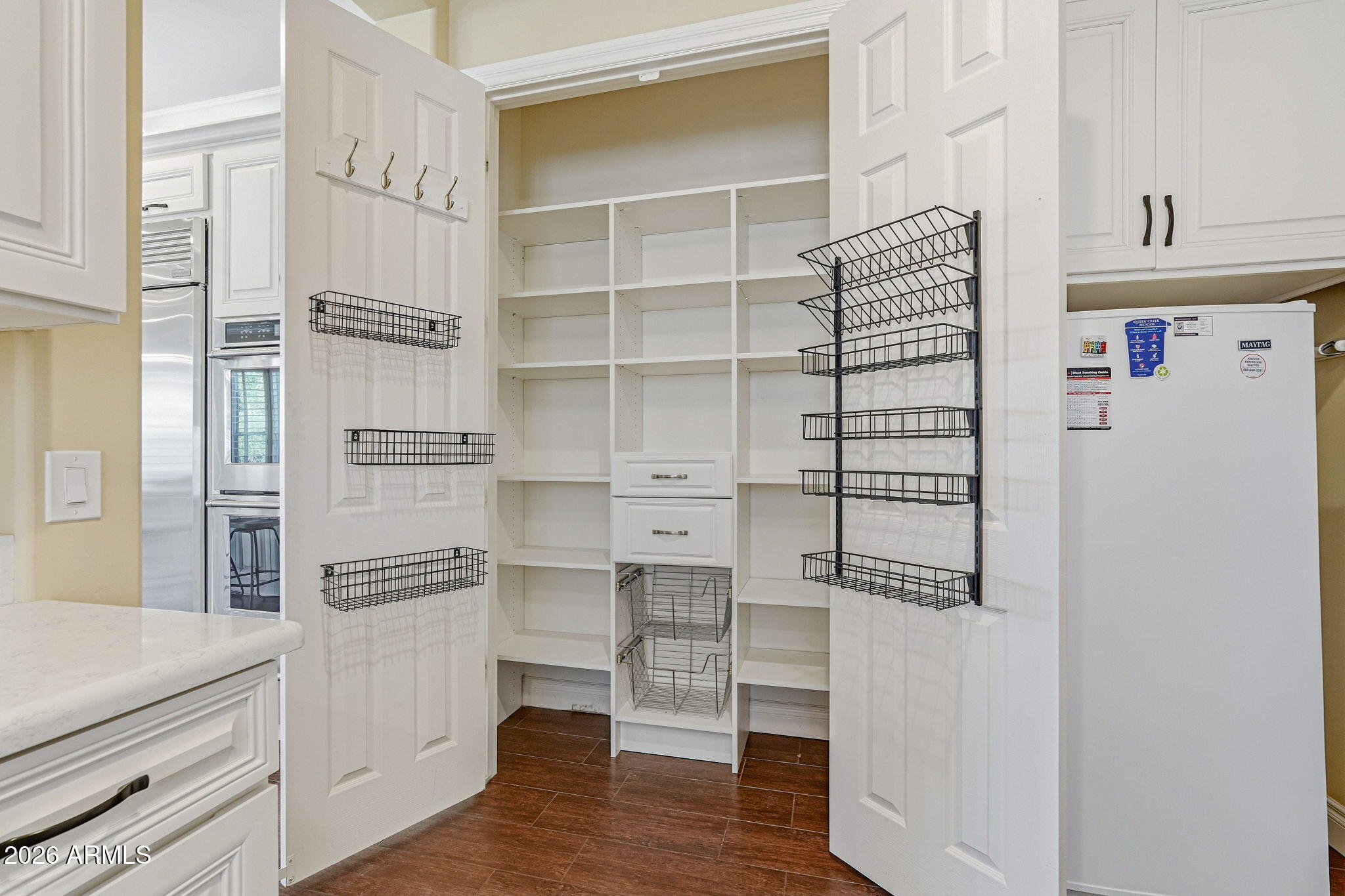 Walk-in pantry with built-in white shelves, wire door baskets, and dark tile flooring.