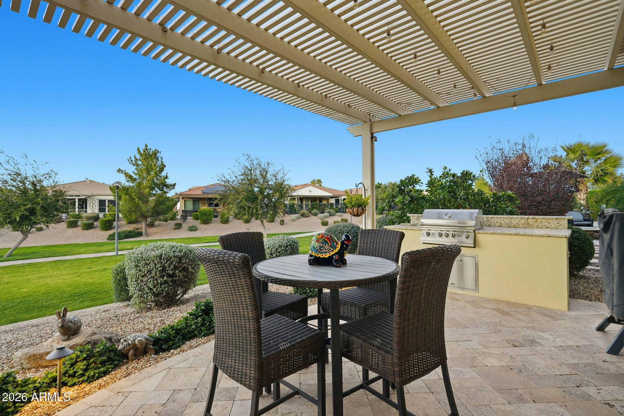 Covered patio with wicker dining set and built-in grill beneath a pergola.