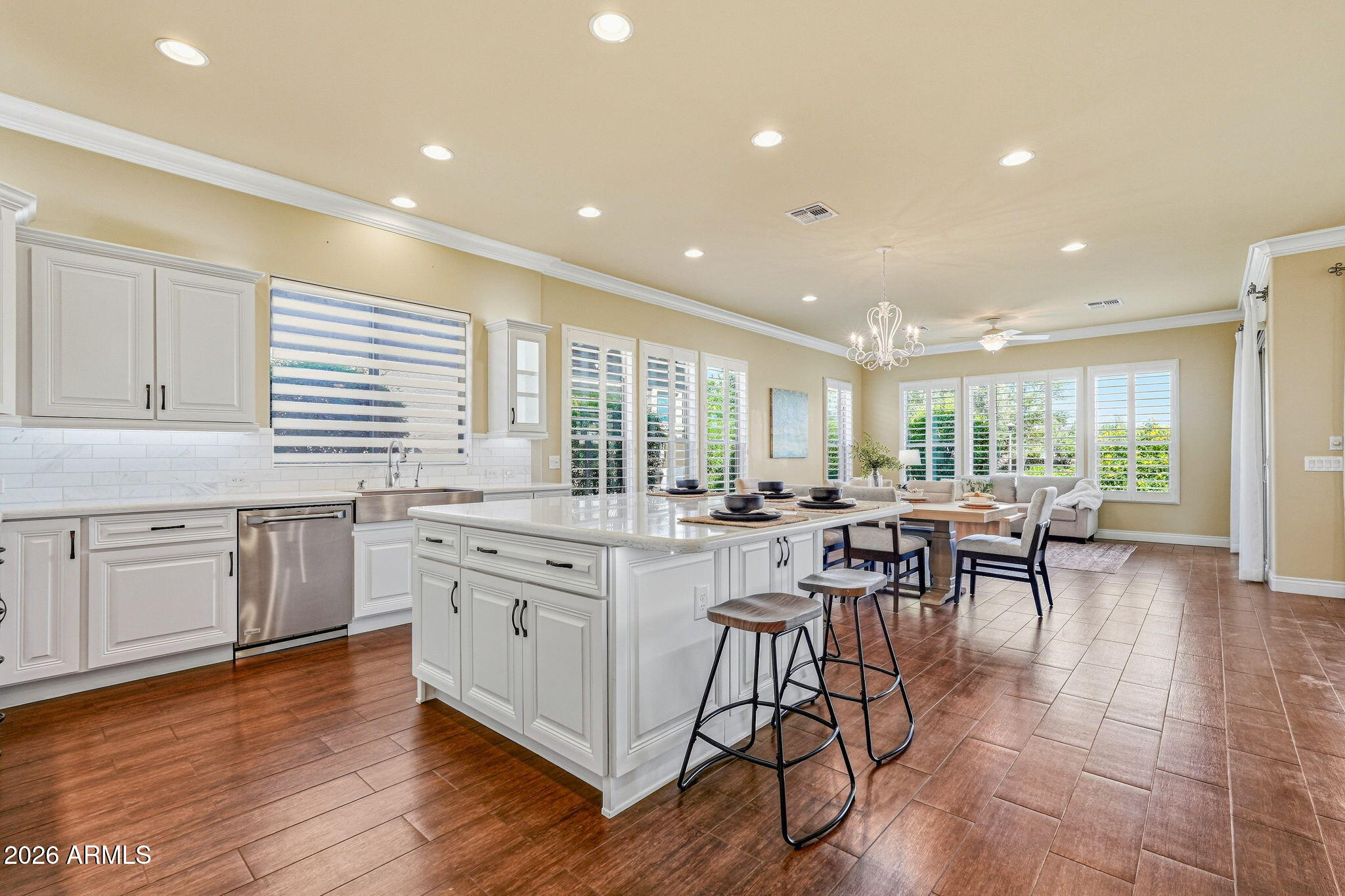 Bright kitchen with a large white island, bar stools, and plantation shutters opening to a dining area.