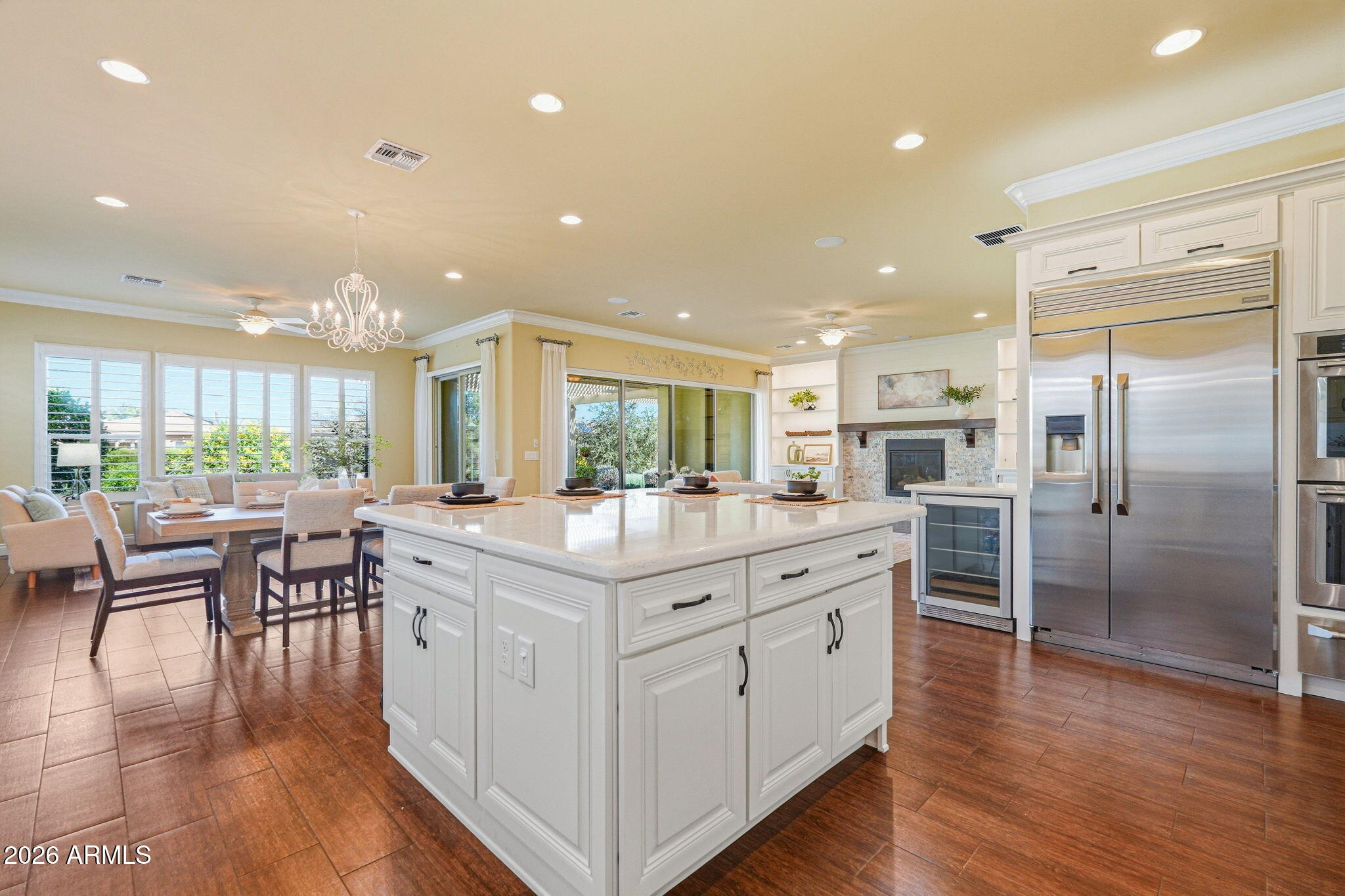 Open-plan kitchen with a large white island, stainless steel refrigerator, and adjoining living area with a fireplace.