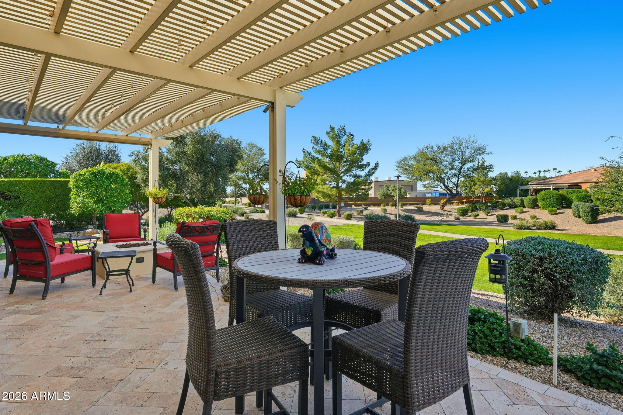 Covered patio with pergola, wicker dining set, and red-cushioned chairs overlooking a landscaped yard.