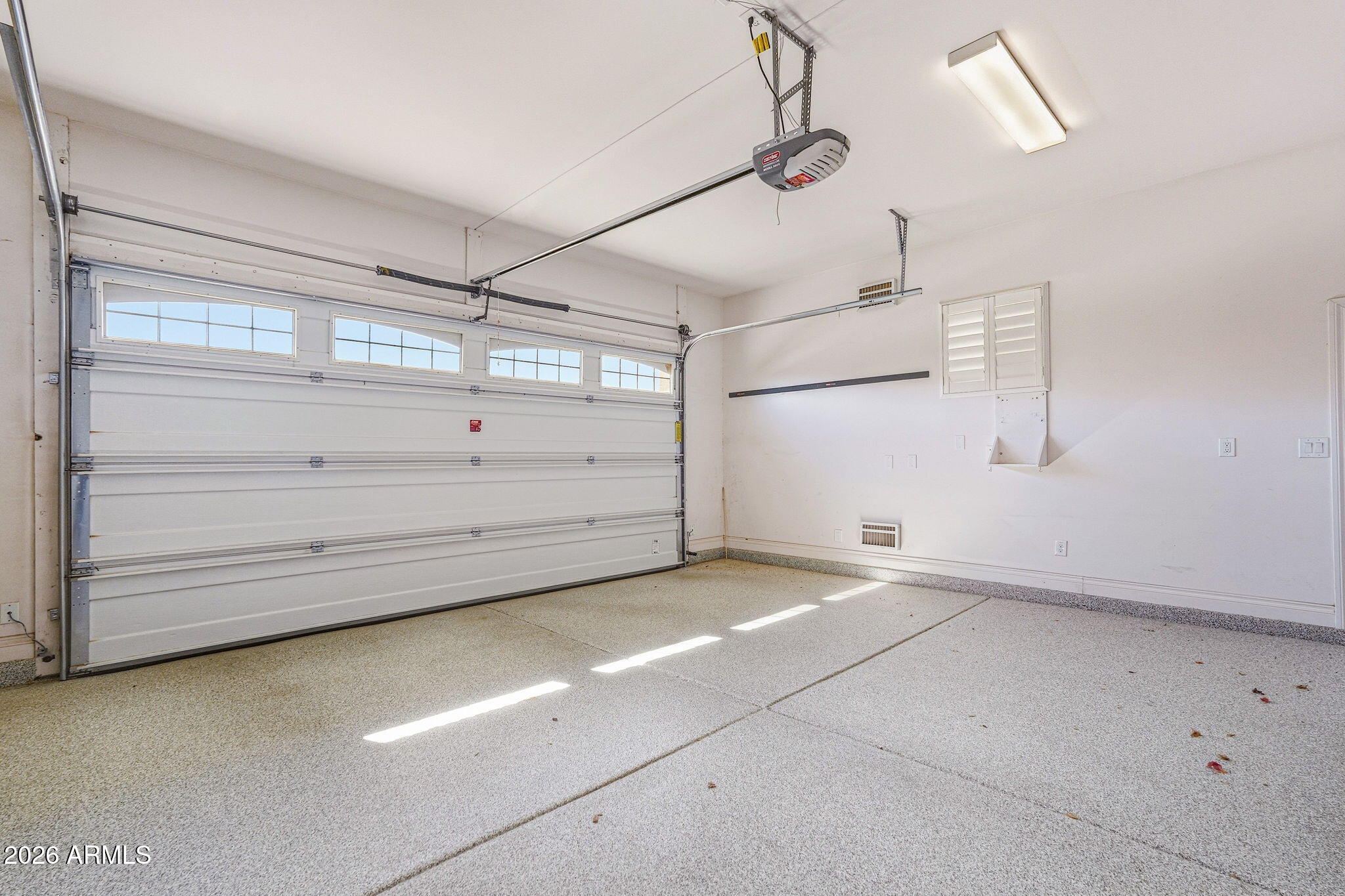 Empty garage with a windowed sectional door and sunlight across its speckled floor.