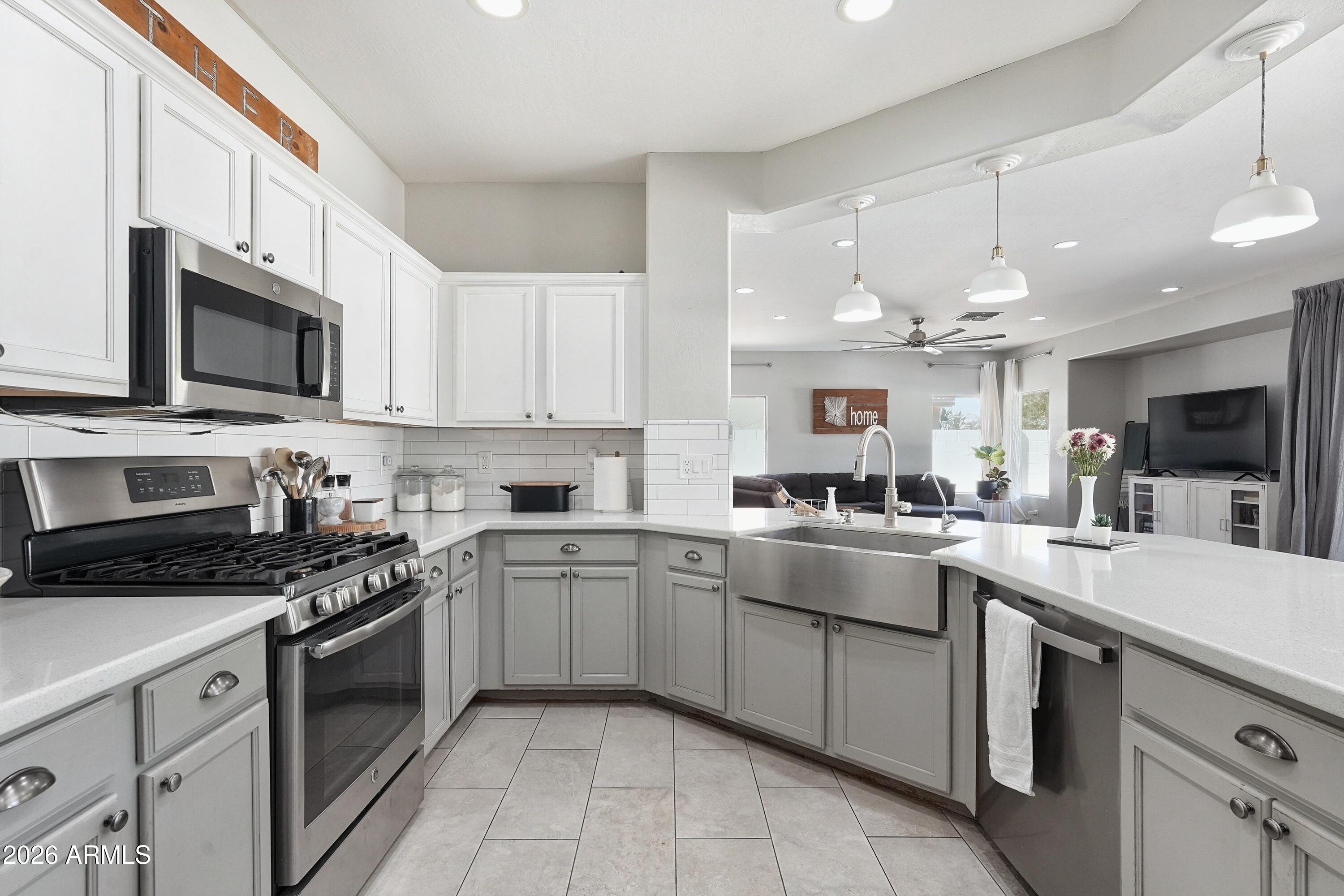 Open-plan kitchen with white cabinets, stainless appliances, quartz counters, and a large sink overlooking the living room.